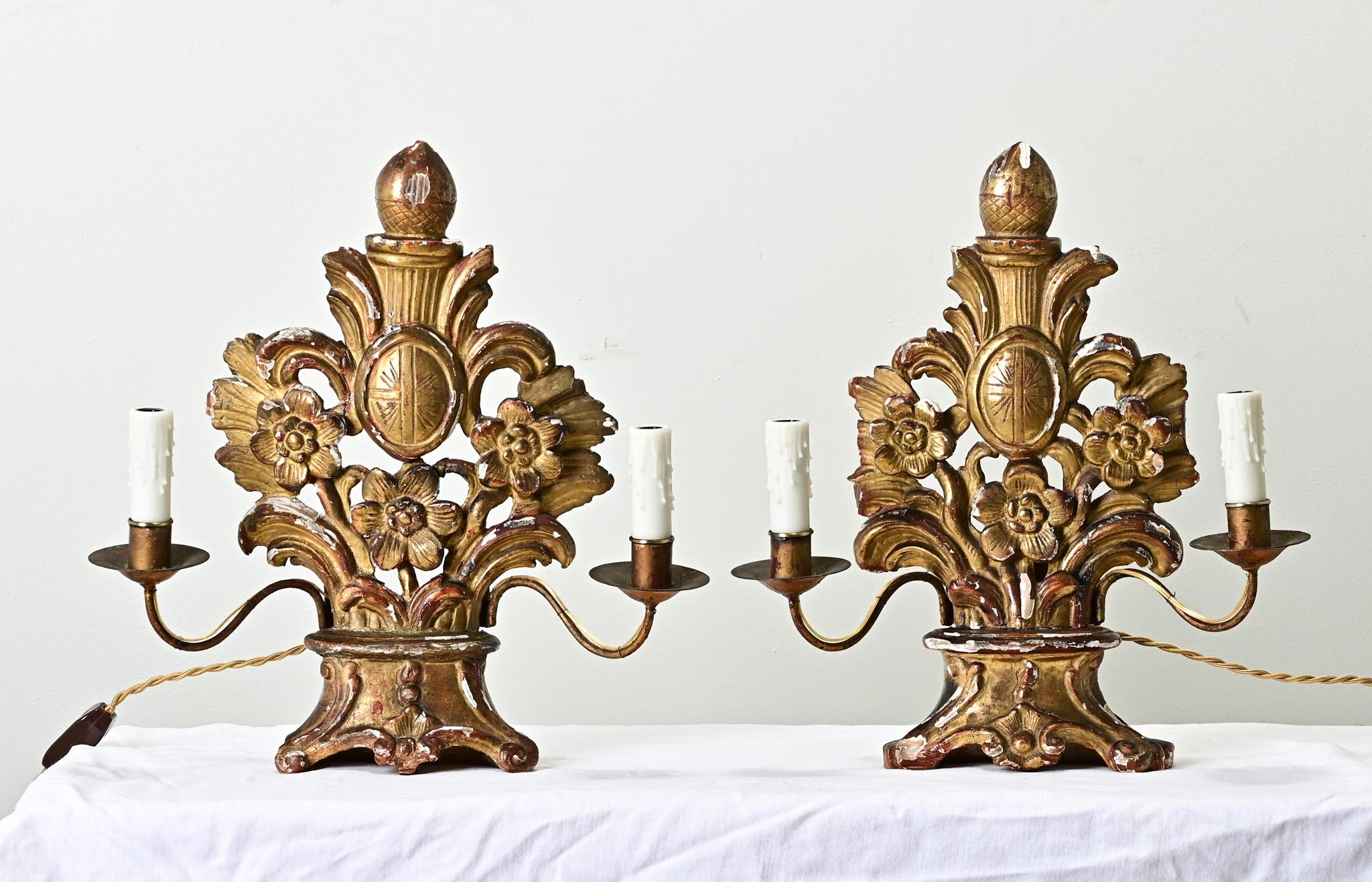 Coppia di candelabri francesi a doppio braccio in legno dorato del 1700. Questa impressionante coppia di lampade intagliate a mano proviene probabilmente da una chiesa. I dettagli intagliati a mano raffigurano steli floreali stilizzati con un