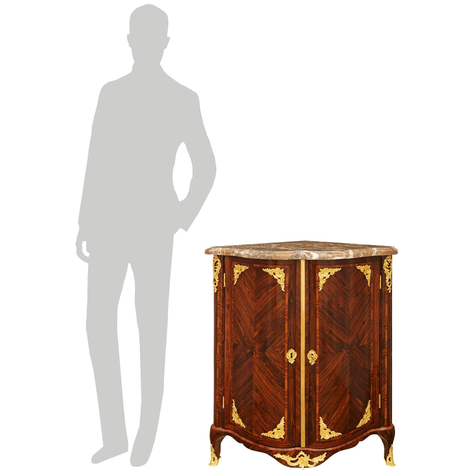 An exceptional and most decorative pair of French 18th century Regence Period Kingwood, Ormolu and Rouge Belge Marble encoignure cabinets. Each unique corner cabinet is raised by most elegant cabriole feet fitted with Ormolu sabots leading up to an
