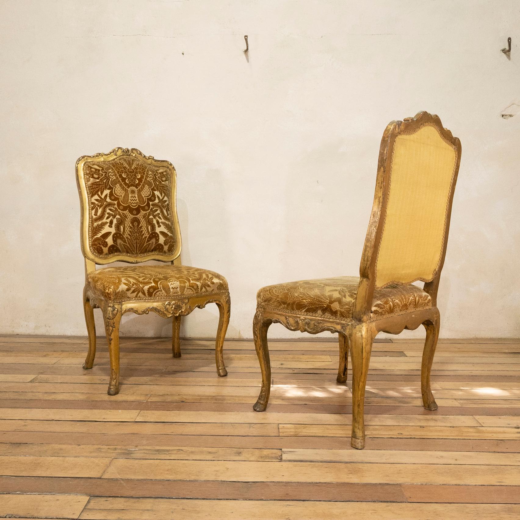 A pair of early 18th century Louis XV chairs. Displaying carved walnut giltwood frames that have worn beautifully over the years - featuring shaped padded backs and seats within foliate carved frames and shell decoration throught. 

Upholstered in