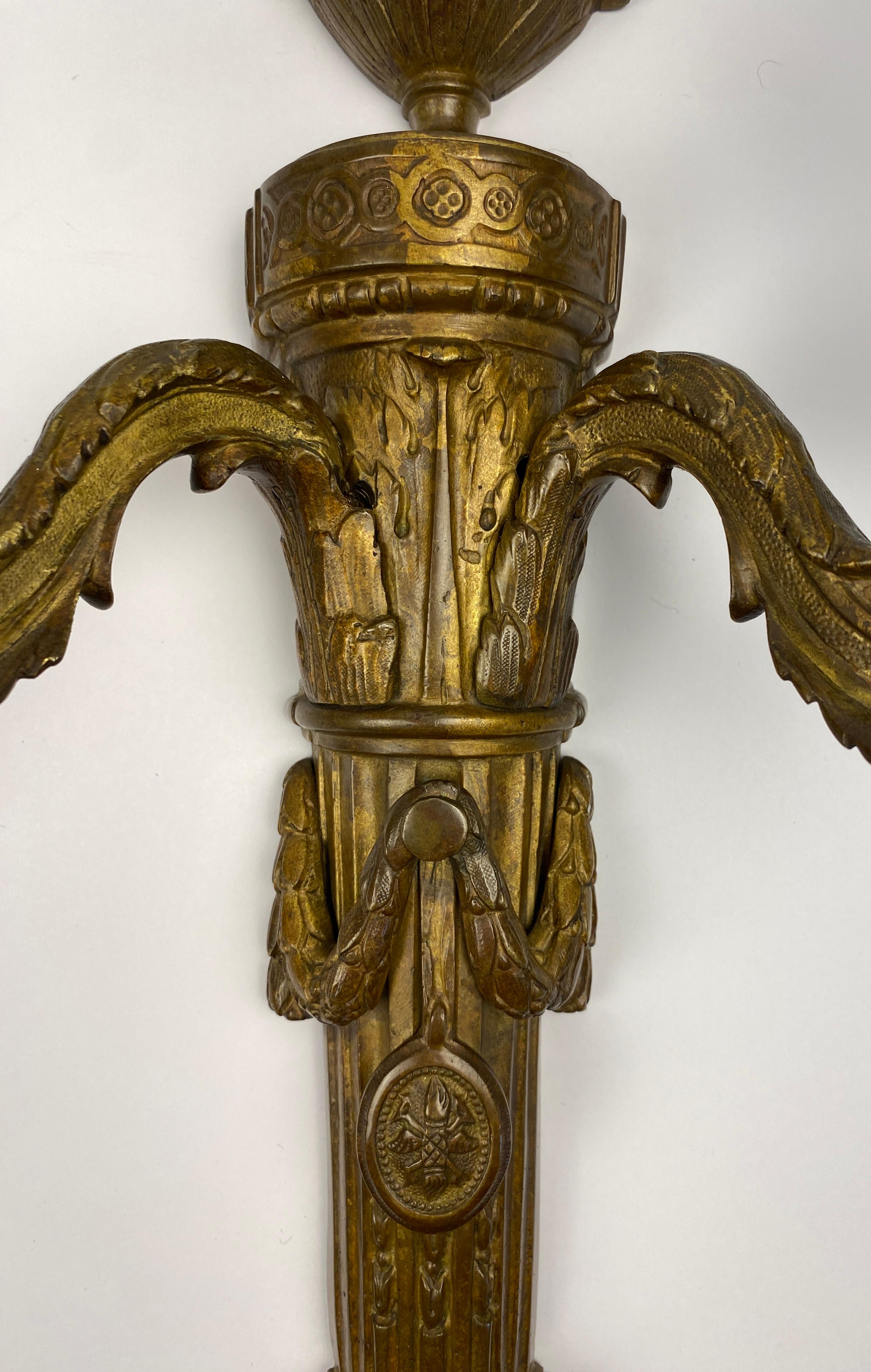 Elegante paire d'appliques en bronze doré de style Louis XVI, à deux bras

Cette paire exquise d'appliques françaises en bronze doré de style Louis XVI, datant de la fin du XVIIIe siècle, témoigne d'un savoir-faire exceptionnel et d'une élégance