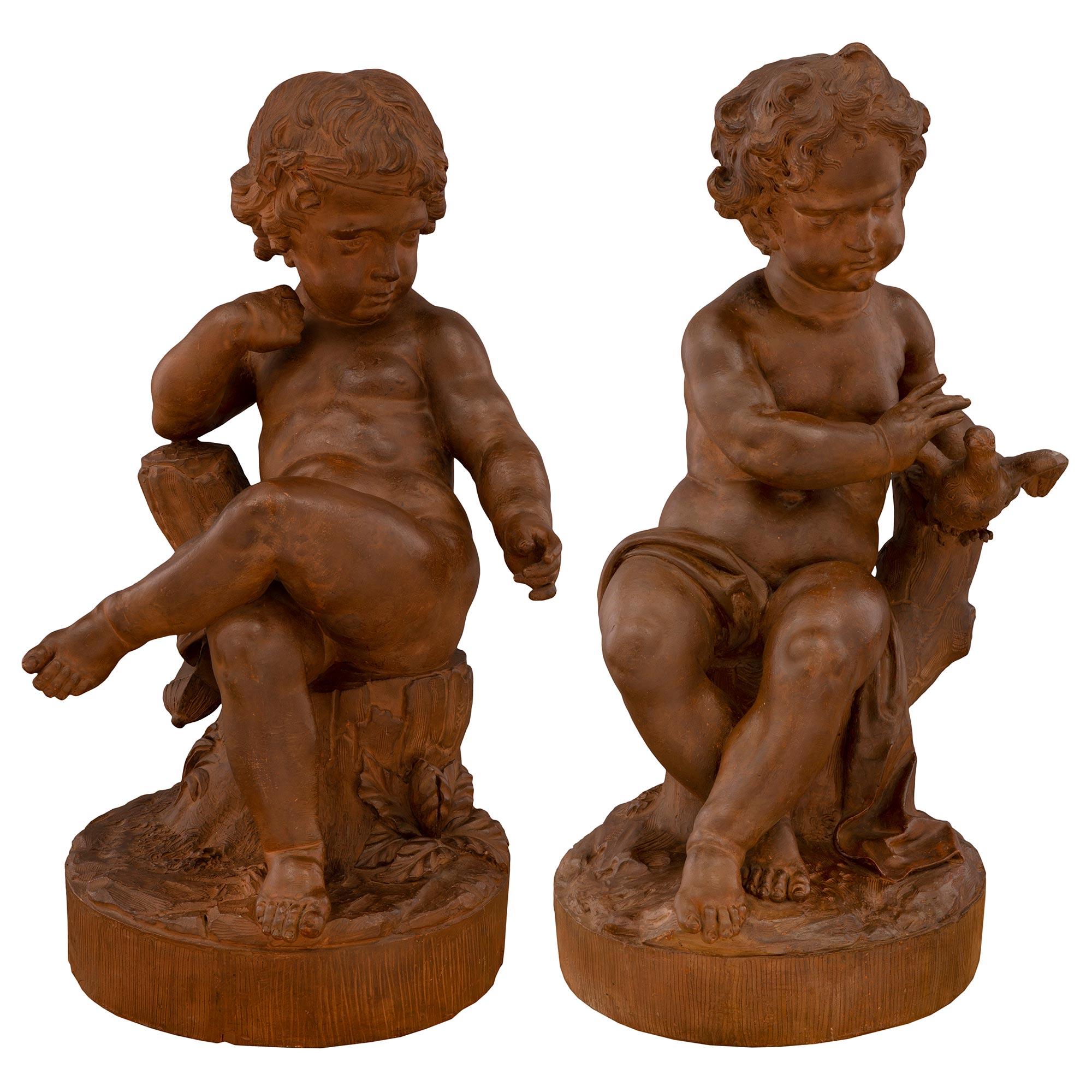 Une paire sensationnelle de statues françaises en terre cuite du 18e siècle représentant de charmants jeunes enfants jouant avec un oiseau. Chaque statue est surélevée par une base circulaire avec un motif semblable à la terre, des fleurs