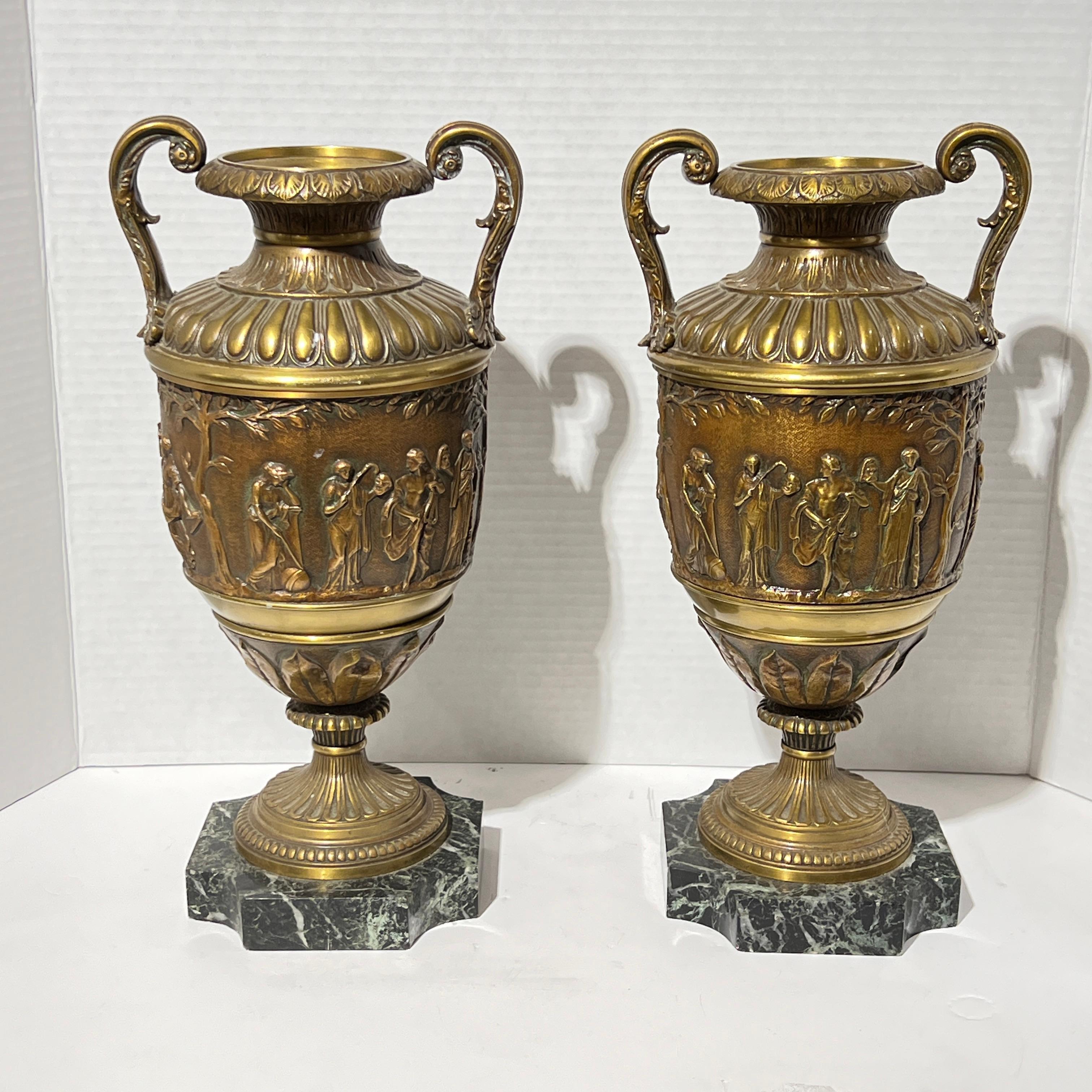 Pair of antique (19th century) bronze urns in the Greco-Roman style with frieze decorated with procession of classical figures, mounted on marble bases.