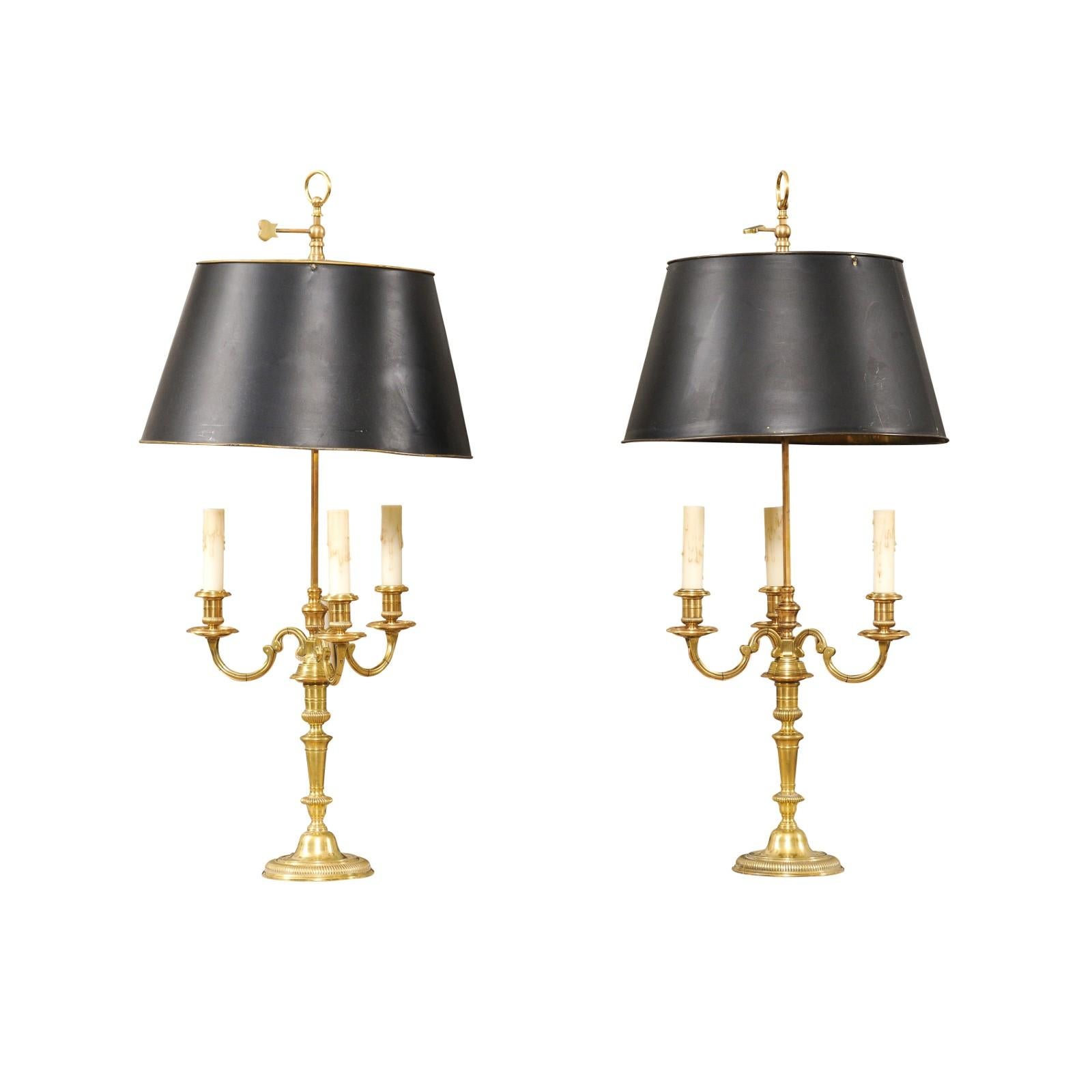 A pair of French turn of the century bronze three-light bouillotte table lamps from the early 20th century with scrolling arms, gadroon motifs and black painted tôle shades. Created in France during the Turn of the Century which saw the transition