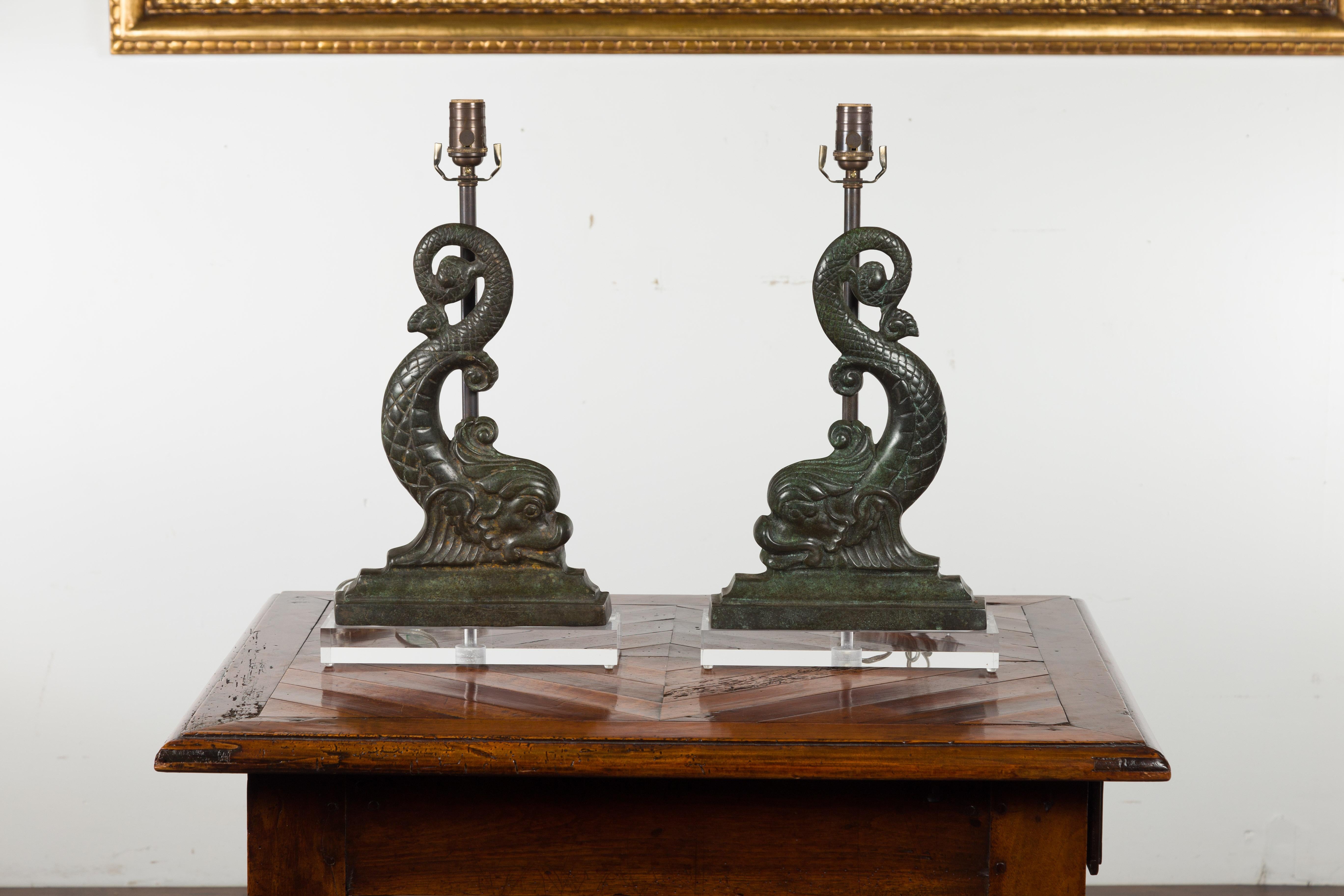 A pair of French Baroque style bronze dolphin table lamps from the early 20th century, with custom Lucite bases. Created in France during the first quarter of the 20th century, each of these bronze sculptures depicts a Baroque style dolphin resting