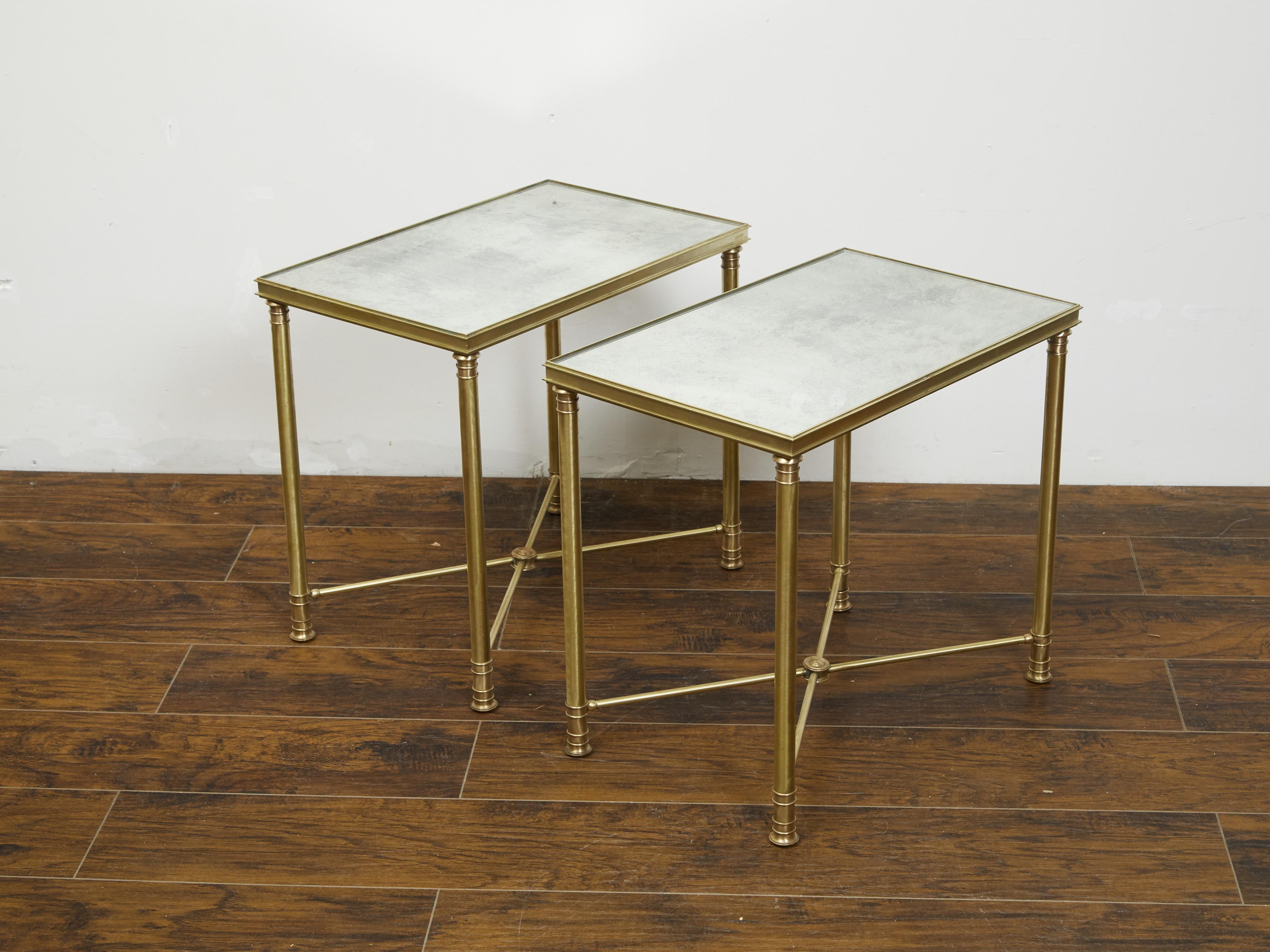 A pair of French bronze side tables from the early 20th century, with mirrored tops and cross stretchers. Created in France during the first quarter of the 20th century, each of this pair of side tables features a rectangular mirrored top sitting