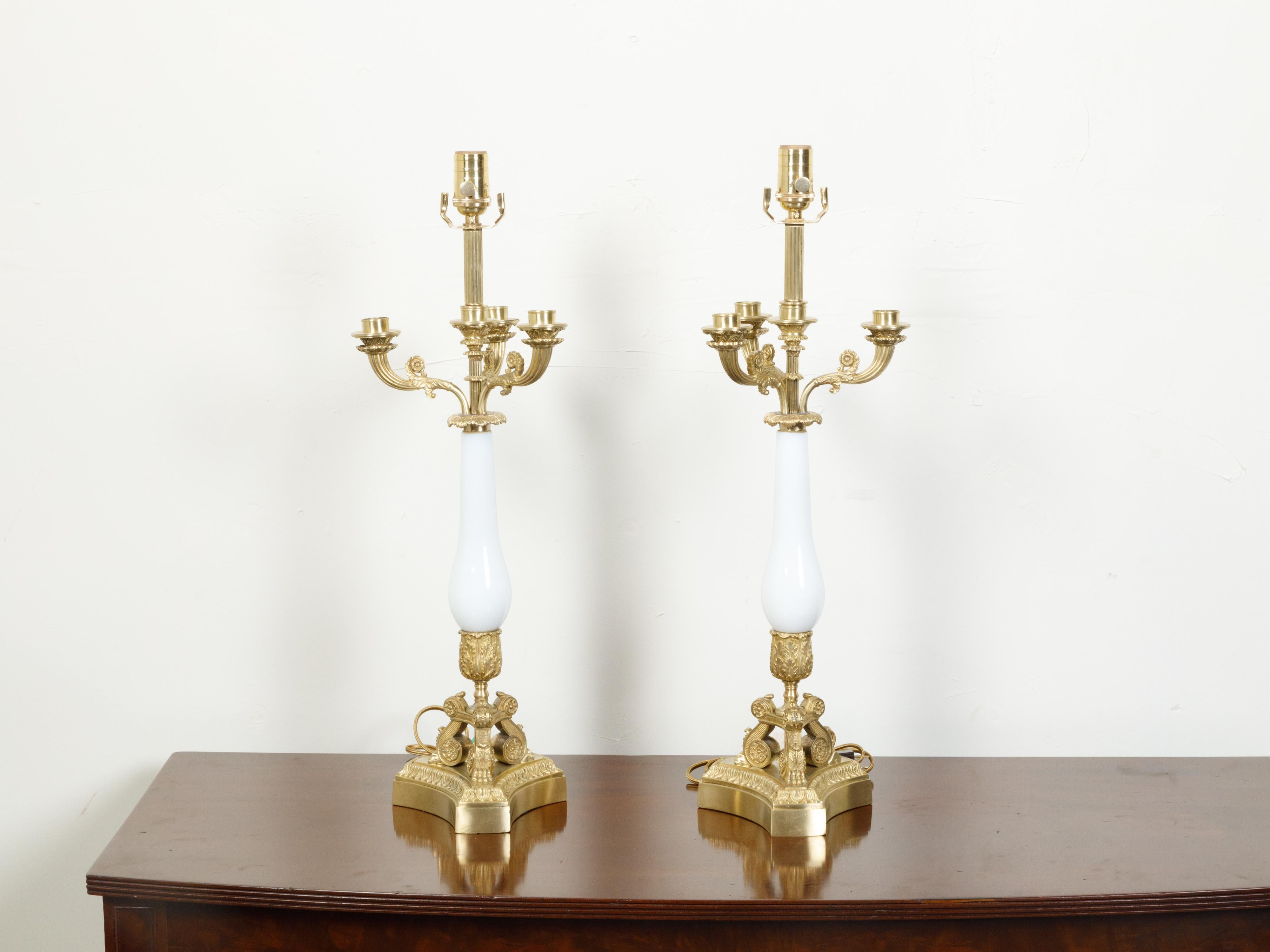 A pair of French Empire style bronze and opaline glass candelabra table lamps from the early 20th century, with scrolling arms and volutes. Created in France during the first quarter of the 20th century, each of this pair of table lamps attracts our