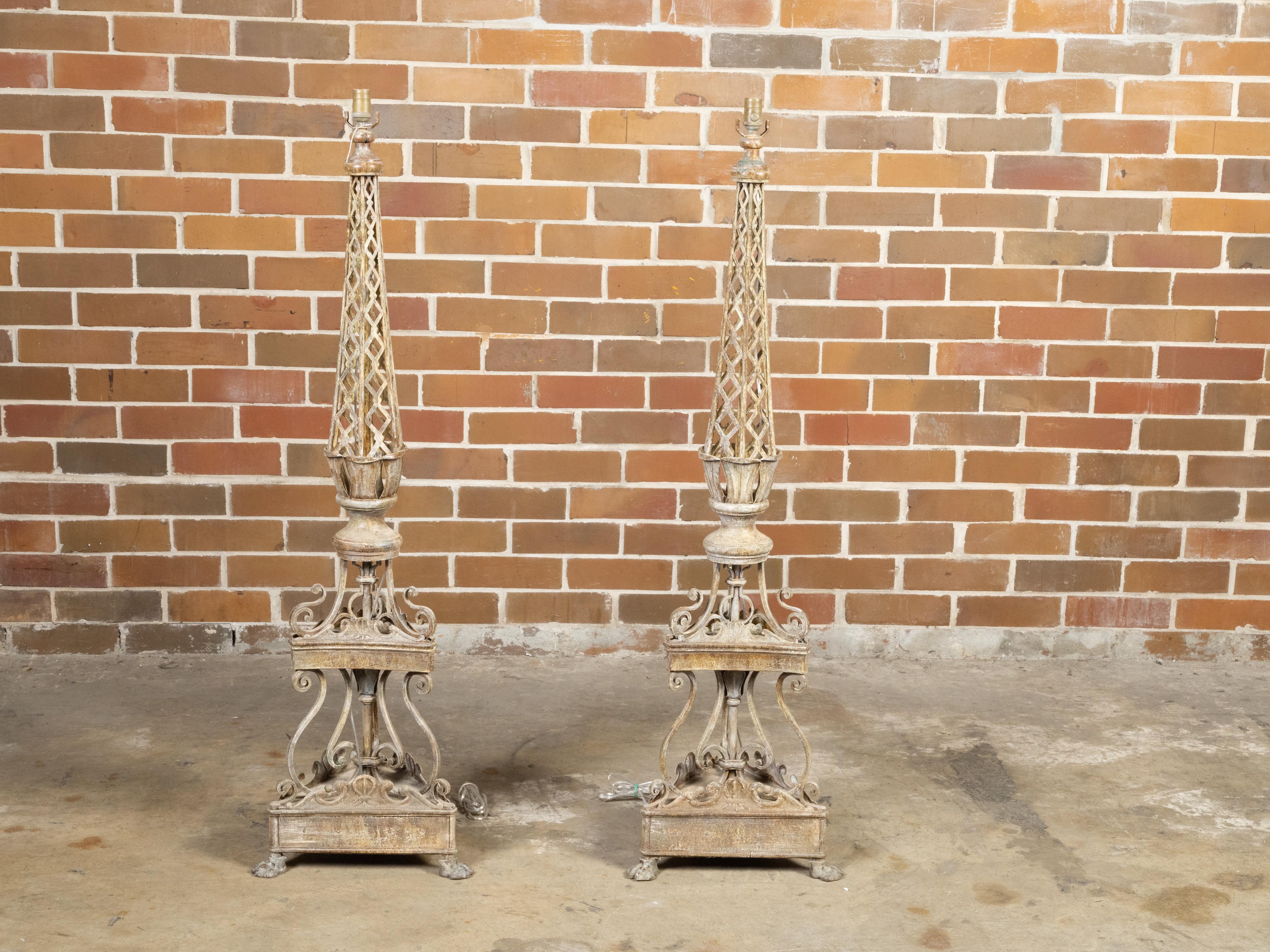 A pair of French painted iron floor lamps from the early 20th century with trellis motifs, tiered scrolling accents and lion paw feet. Created in France in the first quarter of the 20th century during the period called the Années Folles (the Roaring
