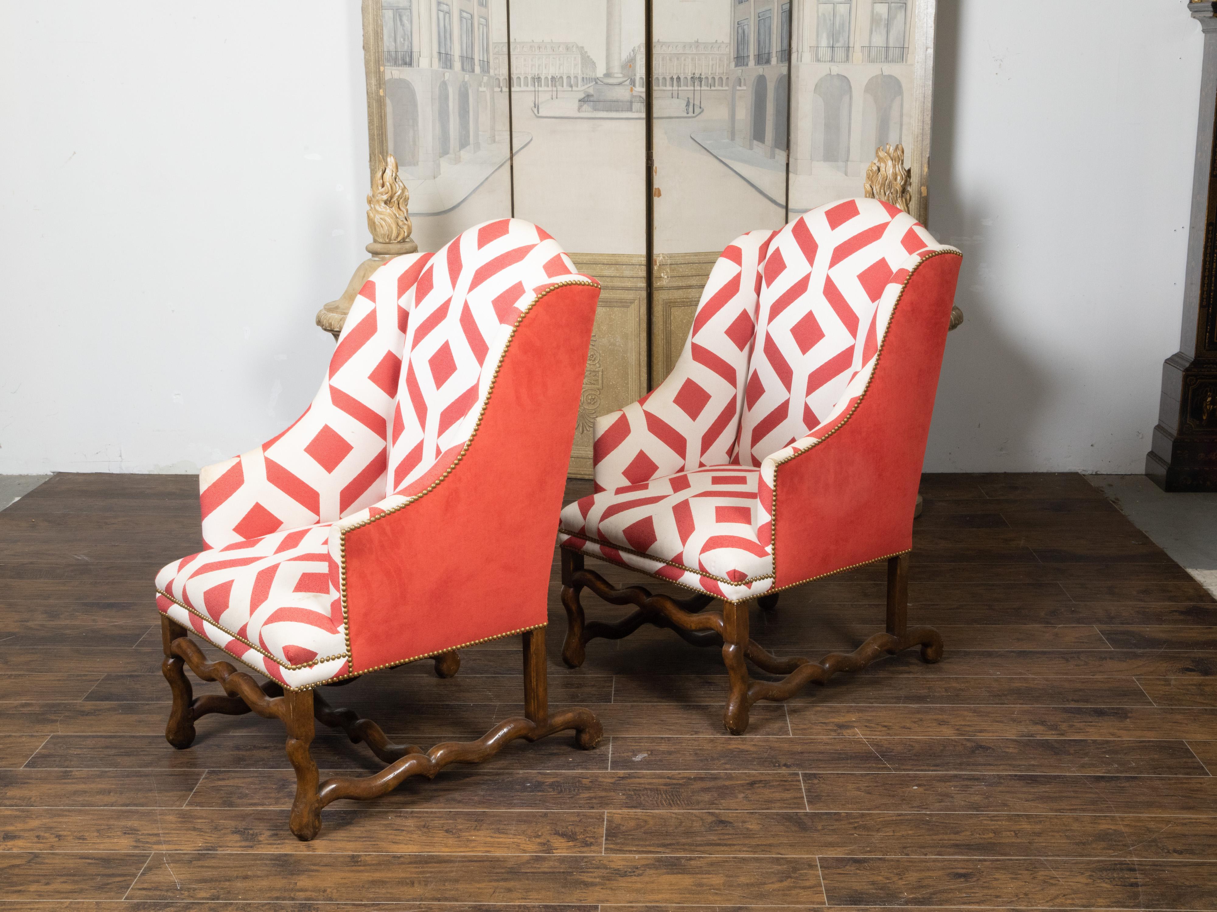 A pair of French wingback chairs from the early 20th century, with Louis XIII style os de mouton bases and red and white geometric upholstery. Created in France during the first quarter of the 20th century, each of this pair of armchairs features a