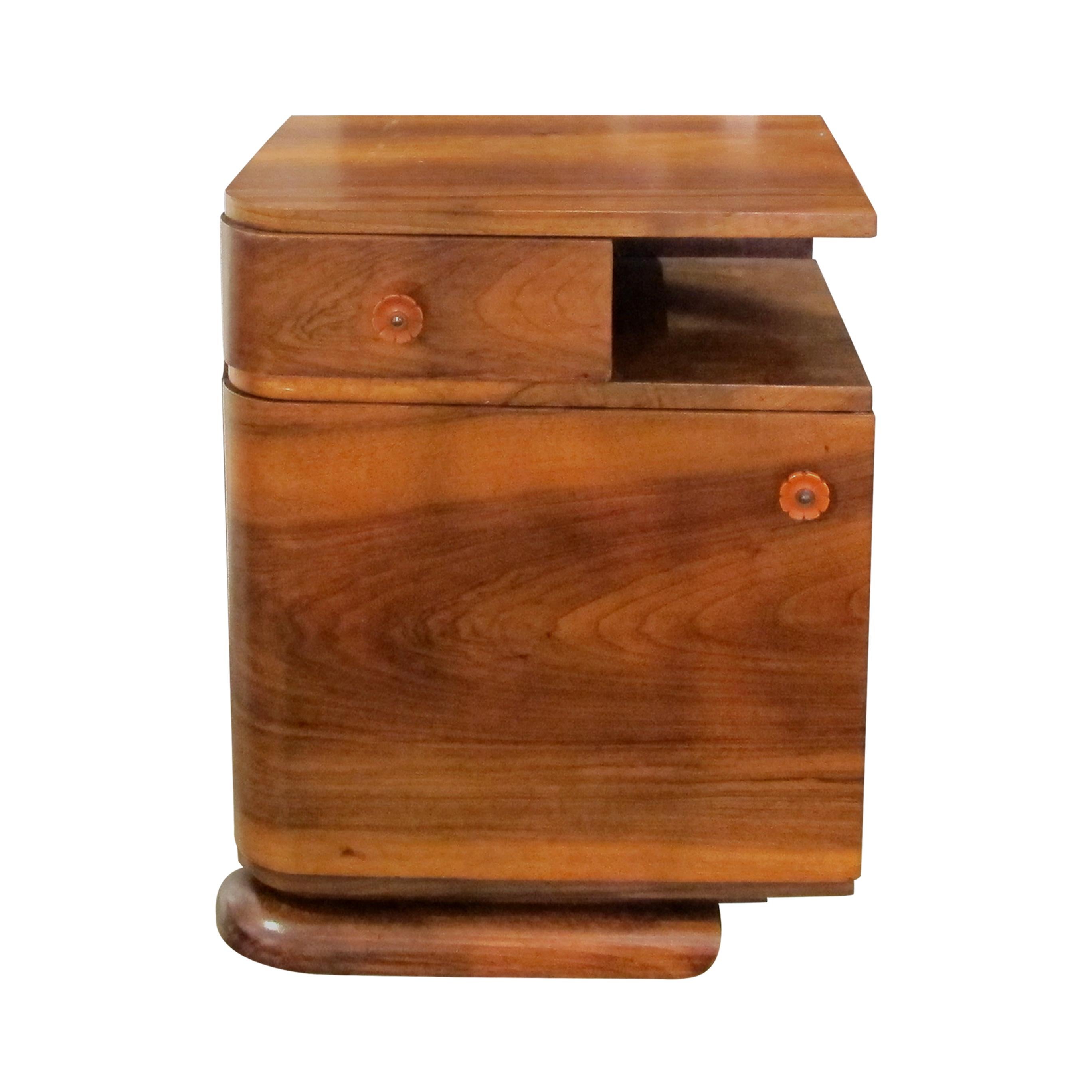 Compact pair of French well-made Art Deco walnut bedside tables with their original orange Bakelite handles. 
Each bedside table boasts a drawer and a large door giving ample storage. The tables are very elegantly presented on a curved long