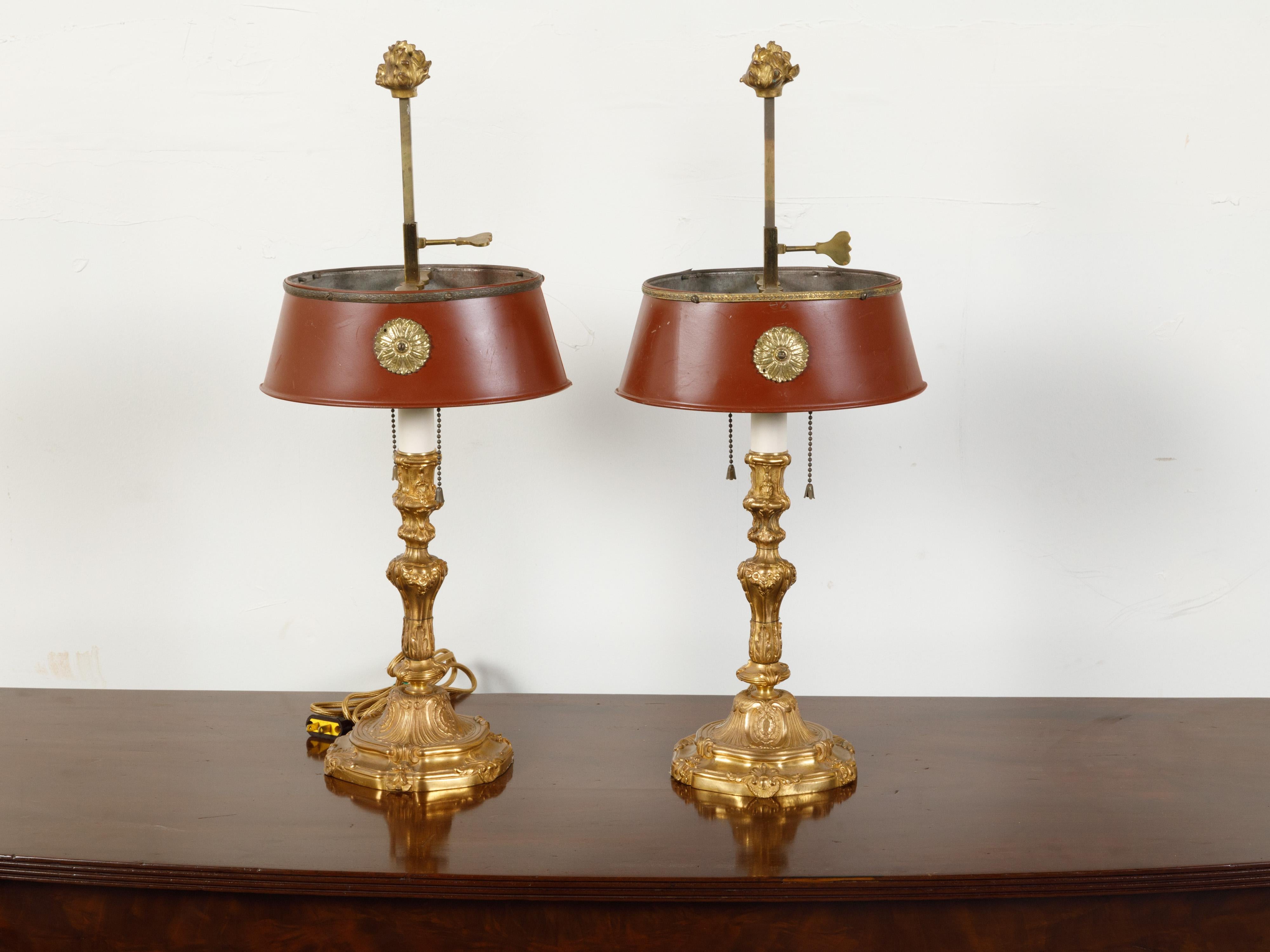 A pair of French gilt bronze table lamps from the first half of the 20th century, with red painted oval tôle shades. Created in France during the 1930s - 1940s, each of this pair of table lamps features a gilt bronze ornate base with flowers and