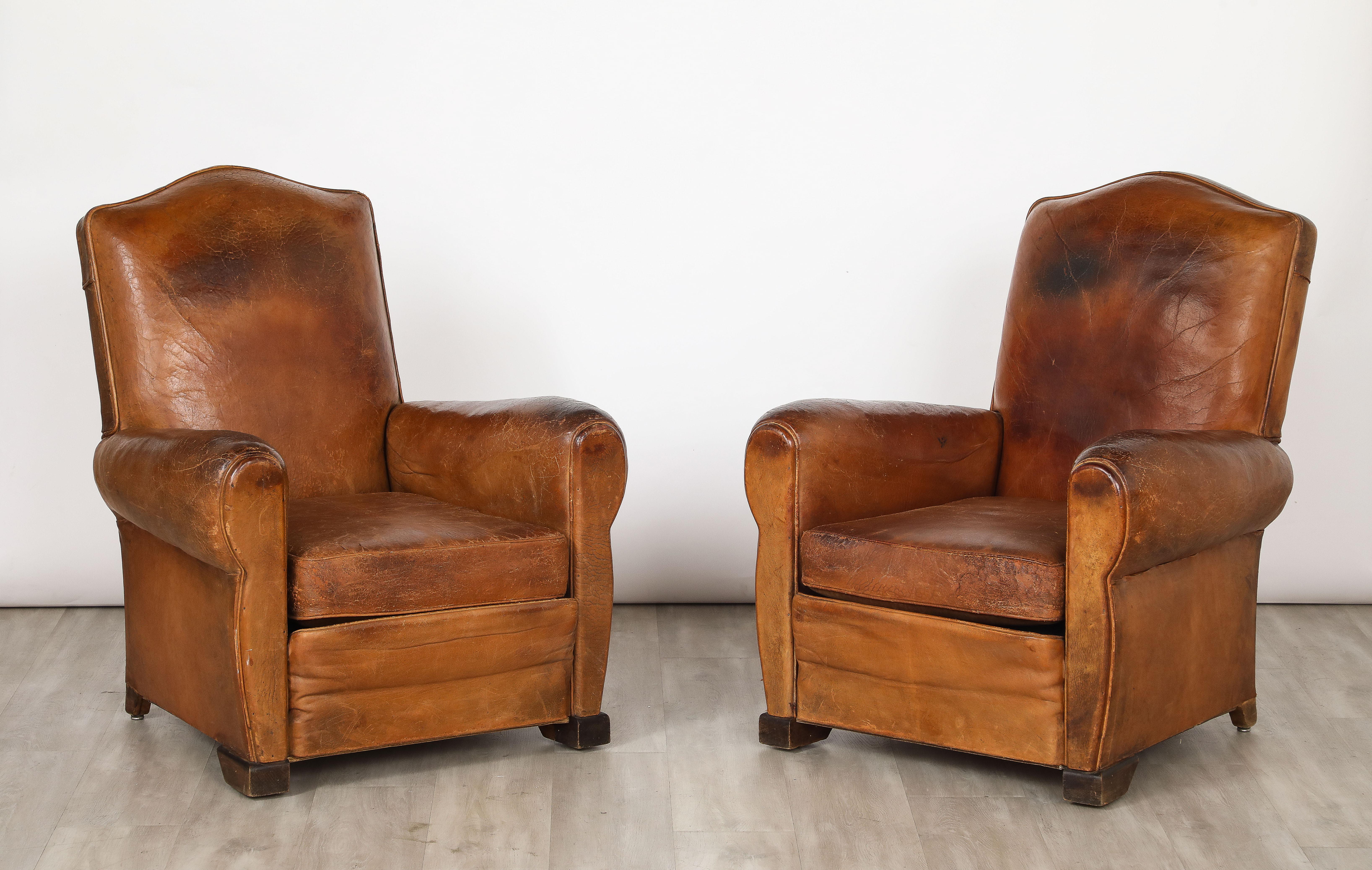 Une magnifique paire de  Fauteuils club en cuir Art Déco français datant des années 1930, avec leur cuir d'origine, le coussin avec un côté tapissé de velours couleur cacao.  L'ensemble repose sur des pieds en bois massif.  Le cuir d'origine est