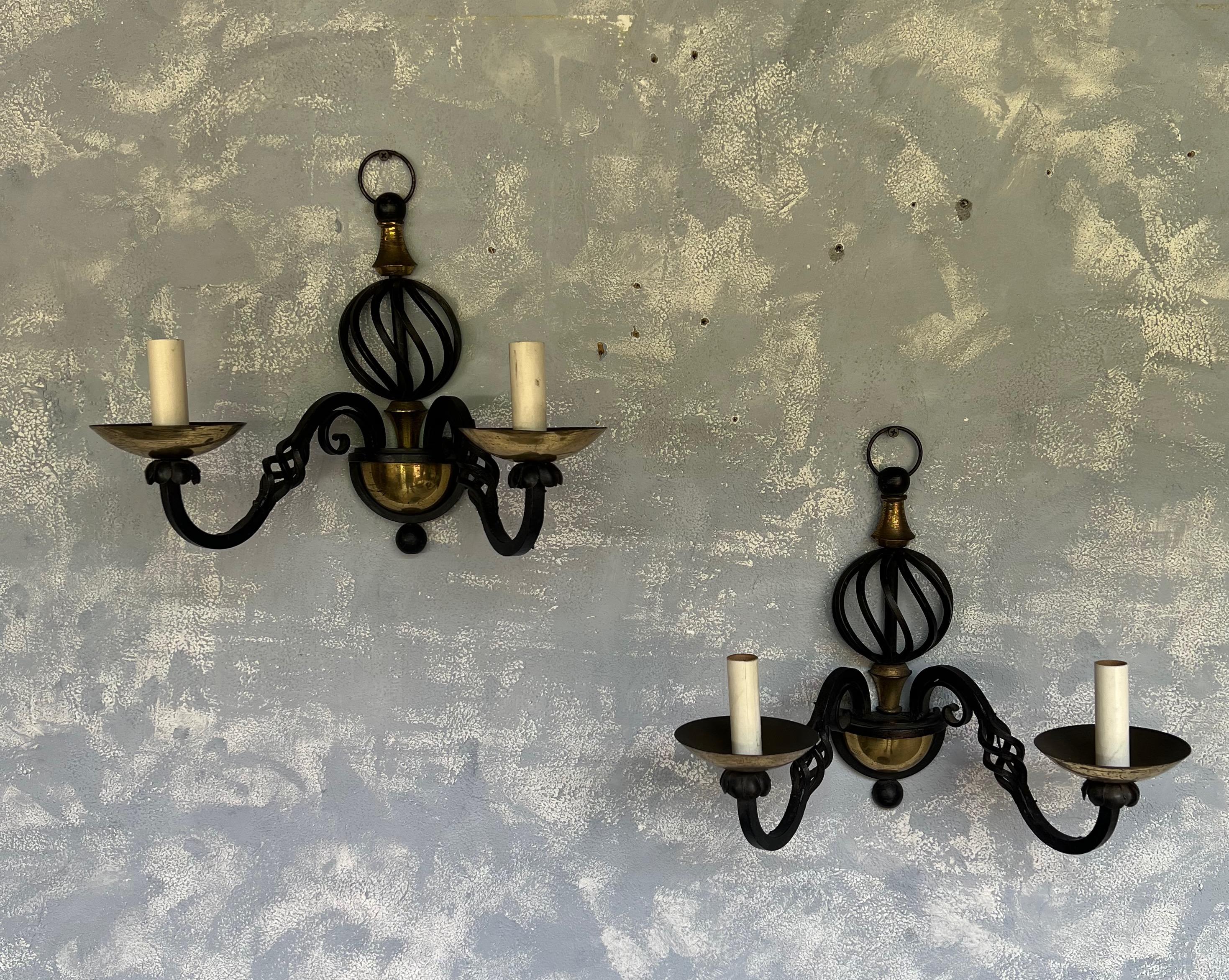 This pair of French 1940s wrought iron and brass double armed sconces adds a touch of vintage sophistication to any space they occupy. The combination of wrought iron and brass offers a striking contrast that catches the eye. These sconces are not