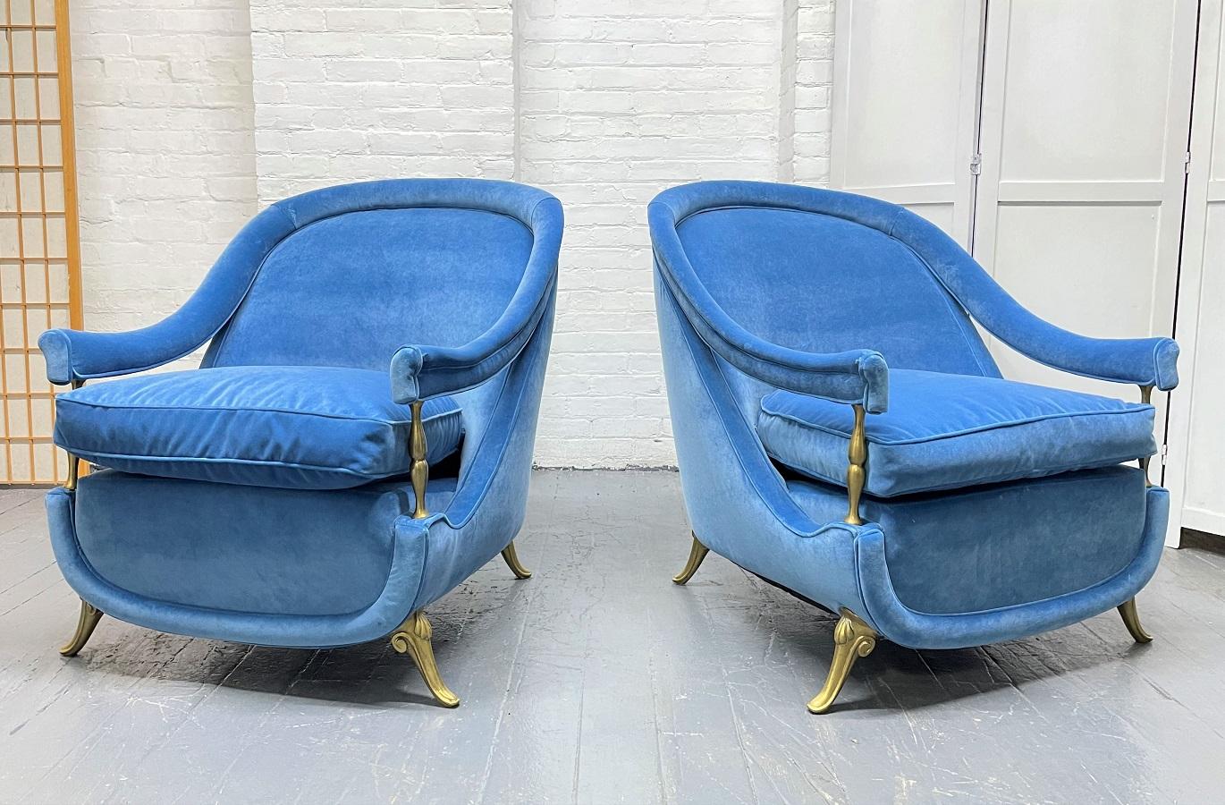 Pair of French 1950s brass and velvet lounge chairs. The chairs have blue velvet upholstery, arched backs, sloping arms, loose cushioned seats with brass feet.