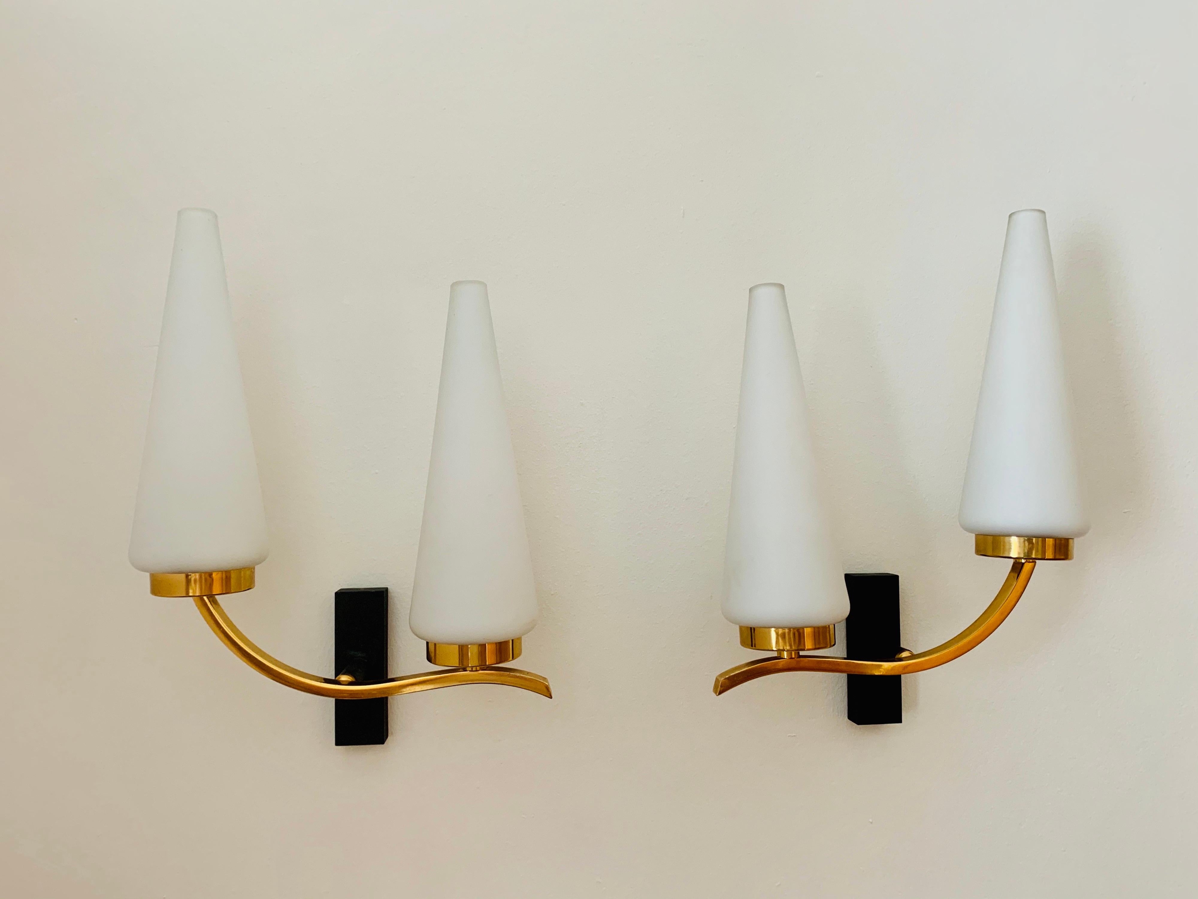 An excellent set of 1950s golden brass sconces composed of two light sources with matte white Opaline glass cone shades.