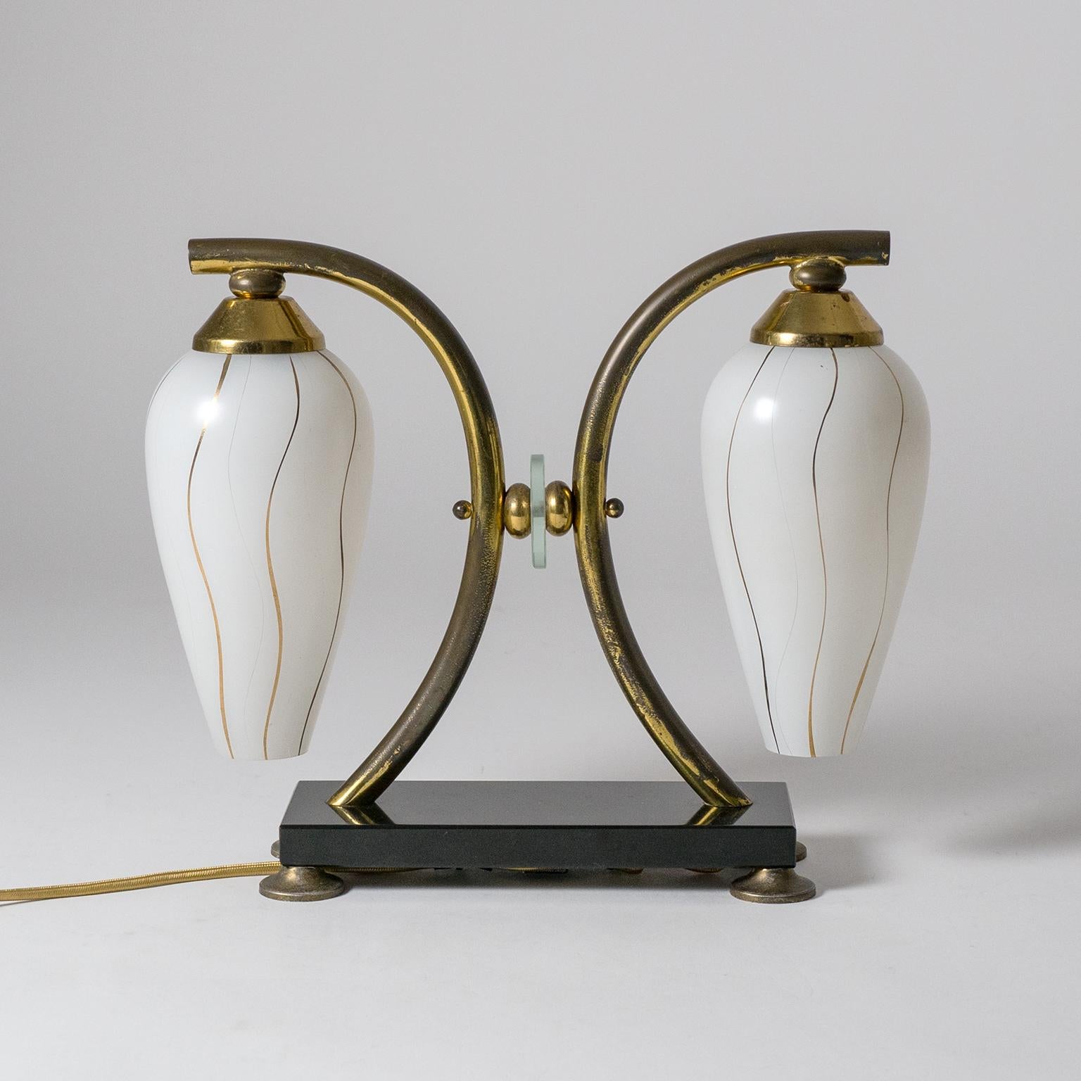 Rare pair of French midcentury table lamps with polished black stone base, brass arms and two enameled glass diffusers. The diffusers are enameled white on the outside with fine incisions and gold paint lines. Fine original condition with a fair