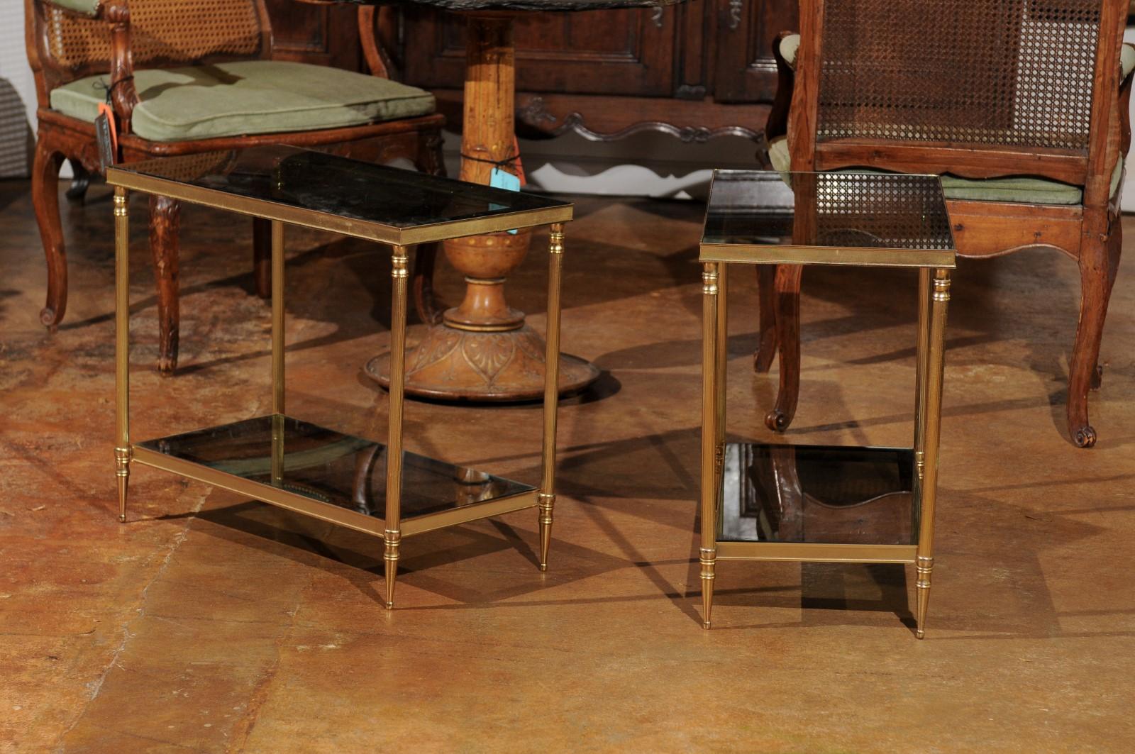 A pair of French vintage brass and glass side tables from the mid-20th century, with lower shelf. Born in France during the midcentury period, each of this pair of French side tables features a rectangular glass top, resting on a brass frame. A