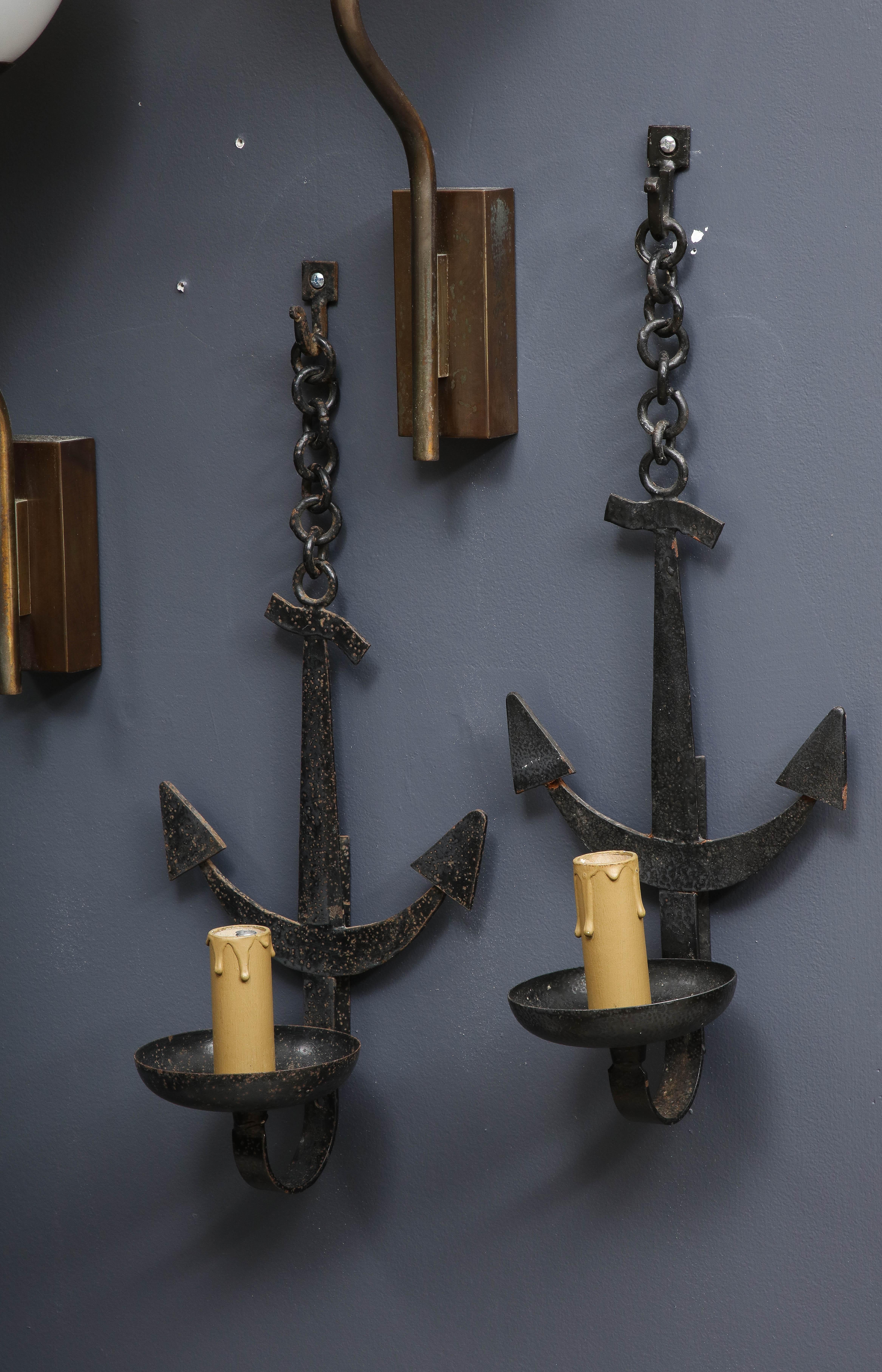 Pair of Brutalist-style midcentury French wrought iron anchor-shaped wall sconces. The anchor hangs from a chain, hooks as shown are included. Each sconce holds a single candle socket. Price includes rewiring for US and repainting
