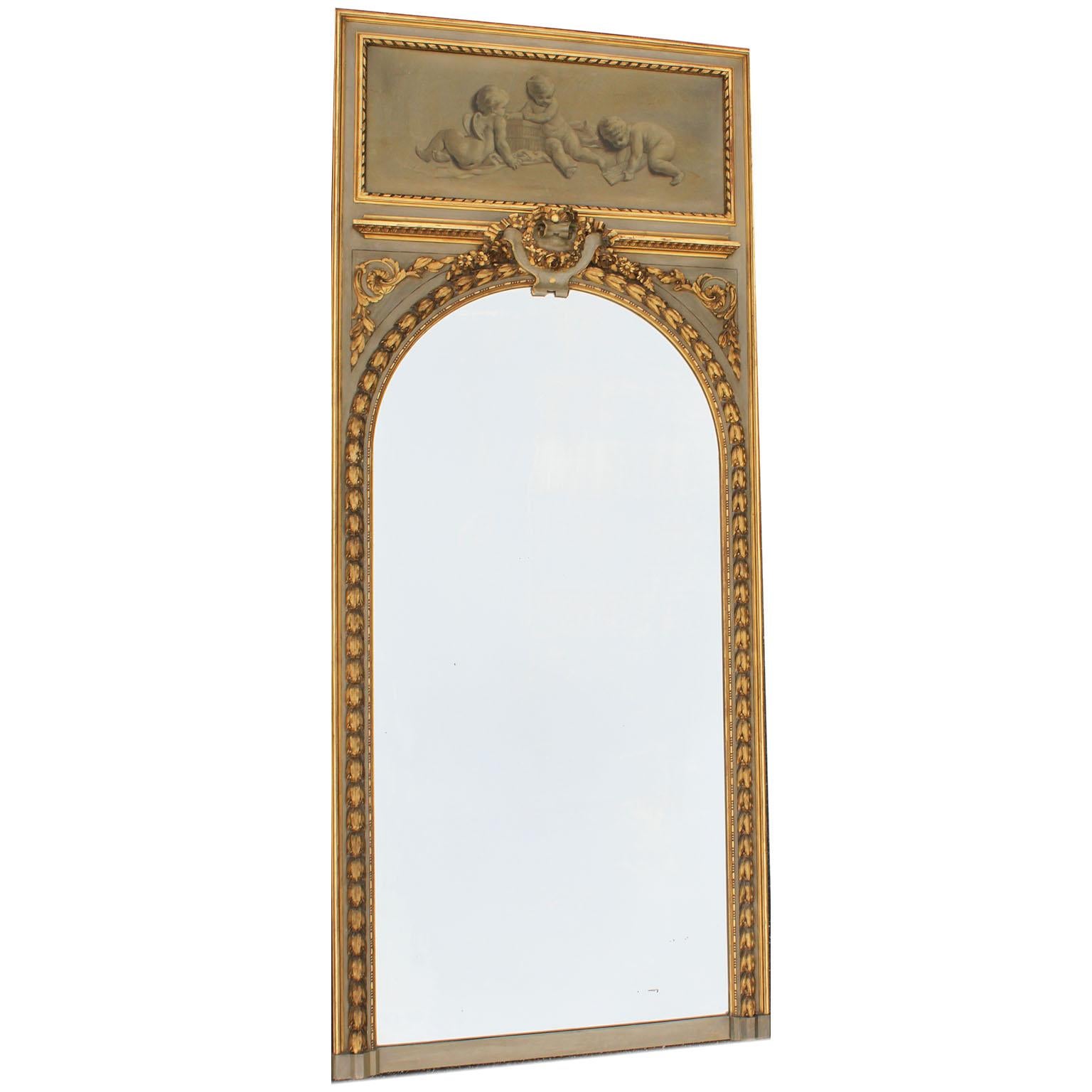 A fine pair of French 19th-20th century Louis XV style grey and parcel giltwood carved trumeau mirror frames. Each frame with an oil on canvas depicting allegorical playful putti and cherubs with a cage, one playing a horn, both within a