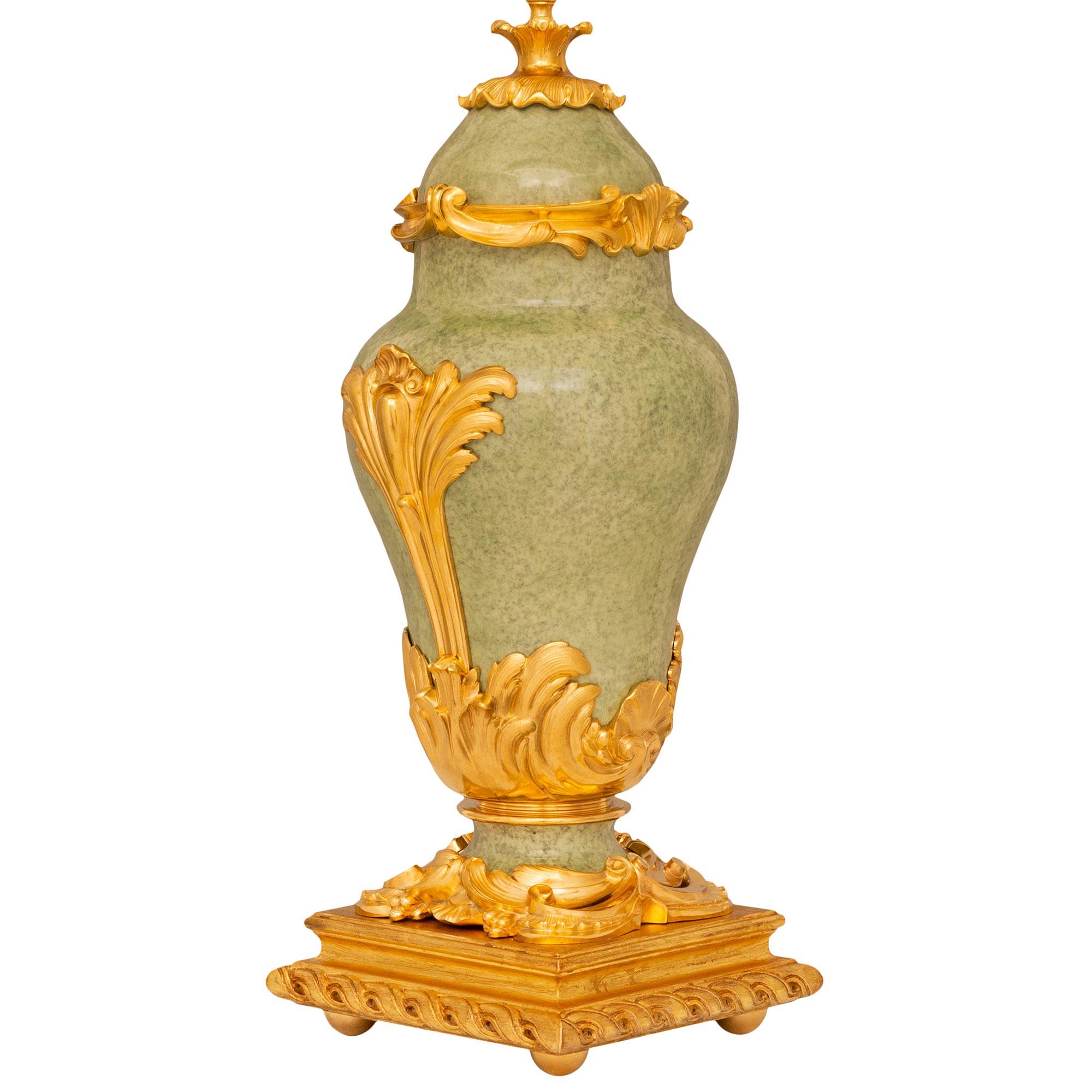 A beautiful and finely detailed pair of French 19th century Louis XV st. light green fire glazed Porcelain, Ormolu, and Giltwood lamps. Each lamp is raised by a square Giltwood platform with a carved spiral design and supported by four round Ormolu