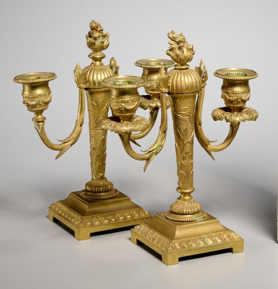 XIX secolo, Francia, coppia di candelabri in bronzo dorato in stile Luigi XVI. Il supporto della colonna, affusolato e cesellato verso l'alto, si erge da una base quadrata. La colonna è sormontata da due coppe di candele che partono da bracci