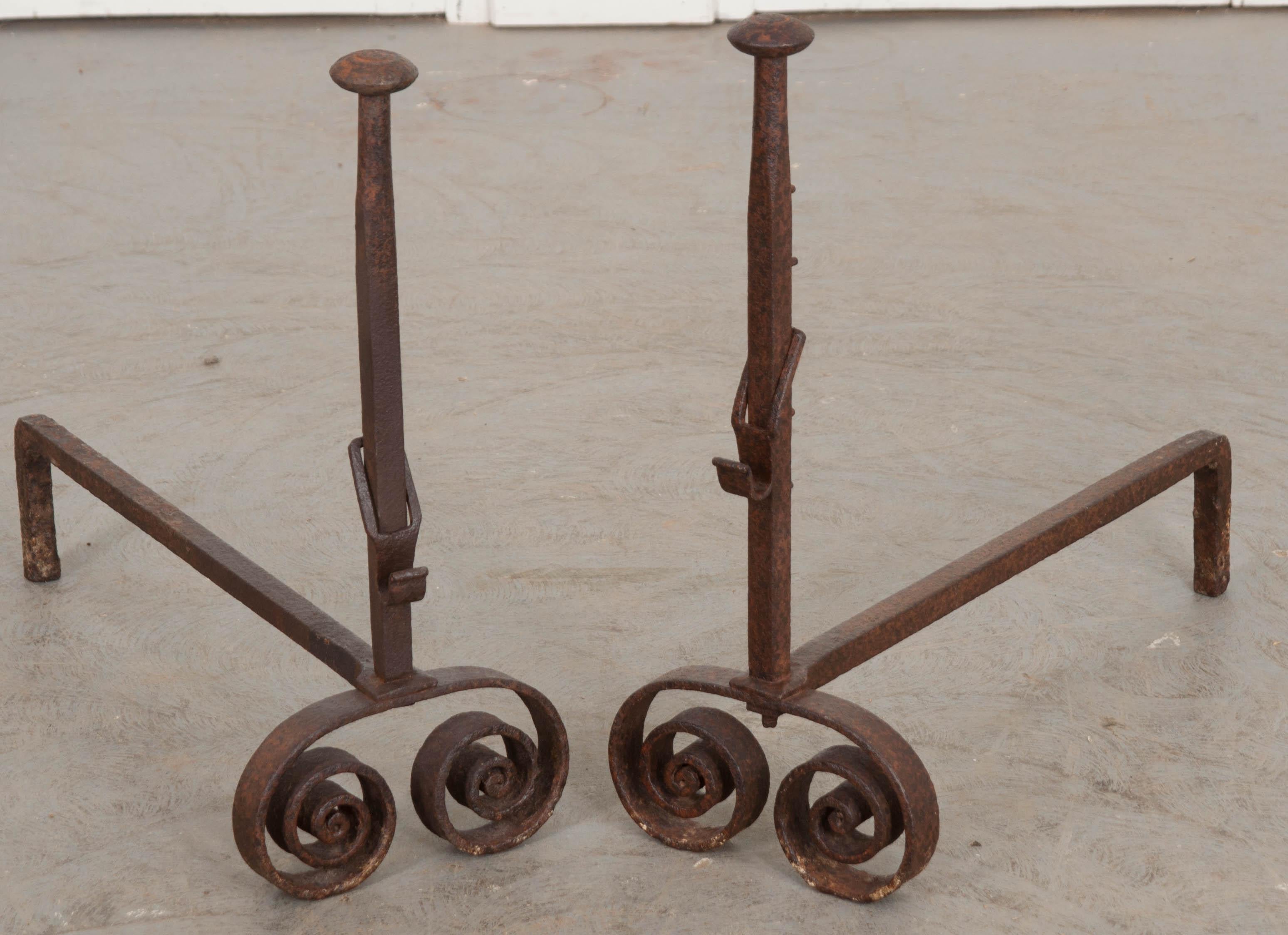 This fine and heavy pair of columnar iron andirons, circa 1850s, was forged in France. Each guard is outfitted with a hook and five ratcheting attachments for hanging pots or spits at varying levels. The iron has taken on a lovely patina thanks to
