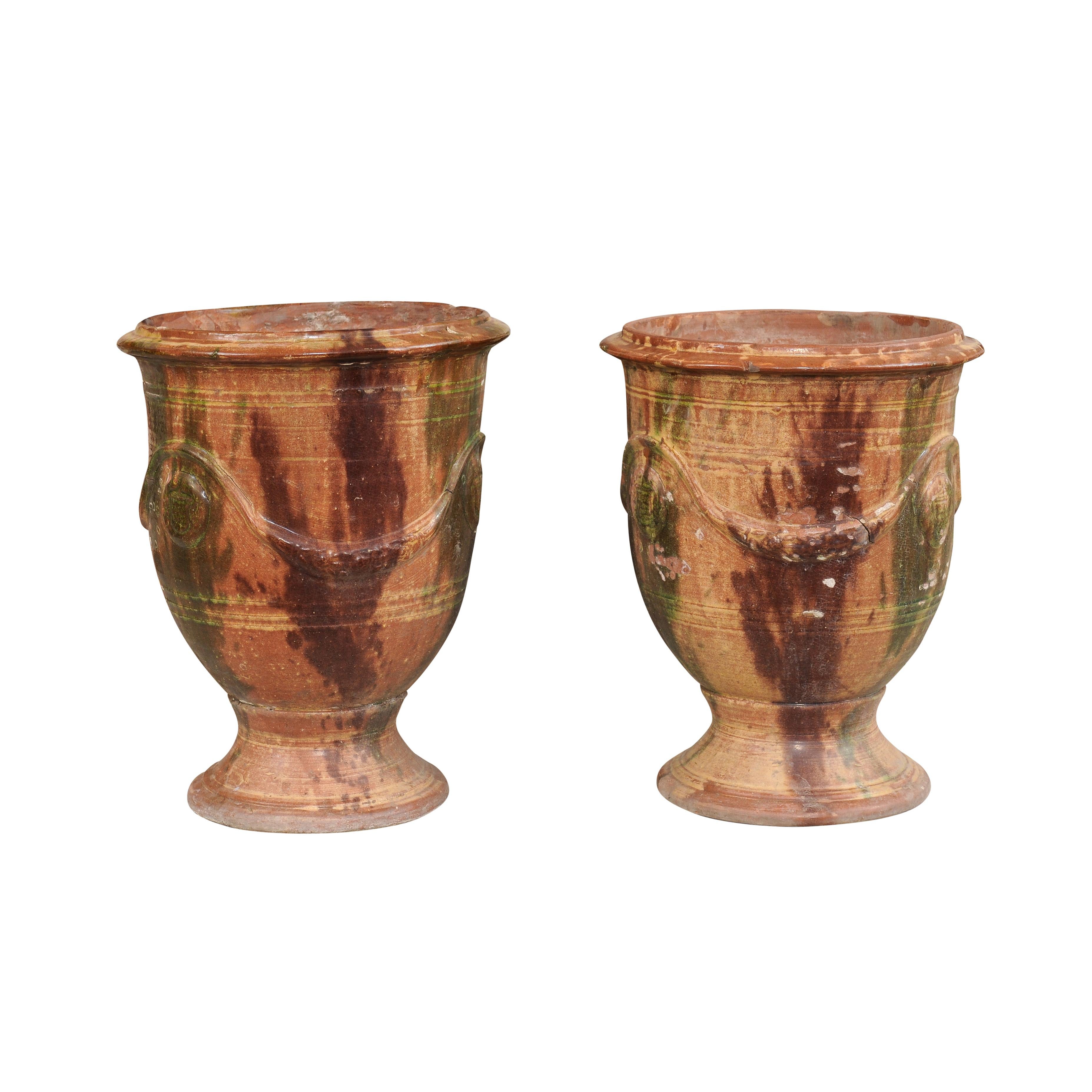 A pair of French Anduze jars from the 19th century with dark brown and green drip glaze and swag decoration in raised relief. Elevate your outdoor space with this captivating pair of 19th-century French Anduze jars. These jars feature a combination