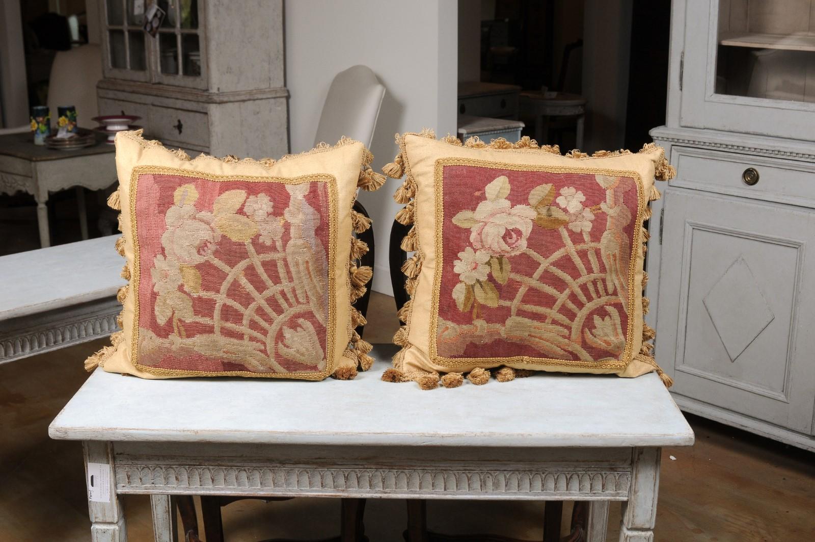 A pair of French Aubusson tapestry pillows from the 19th century, with floral motifs, gallon trim and petite tassels. Created during the 19th century in the Aubusson tapestry manufacture located in central France, each of this pair of pillows