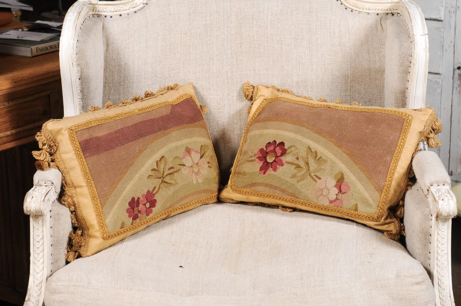 A pair of French Aubusson tapestry pillows from the 19th century, with floral décor and petite tassels. Created in the Aubusson tapestry manufacture located in central France during the 19th century, each of this pair of horizontal pillows features