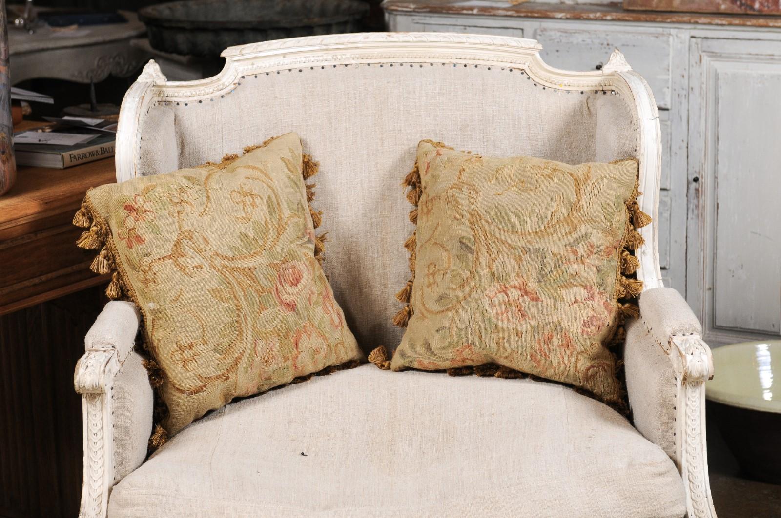 A pair of French square shaped Aubusson tapestry pillows from the 19th century, with floral decor and tassels. Created during the 19th century in the Aubusson tapestry manufacture located in central France, each of these pillows features a delicate