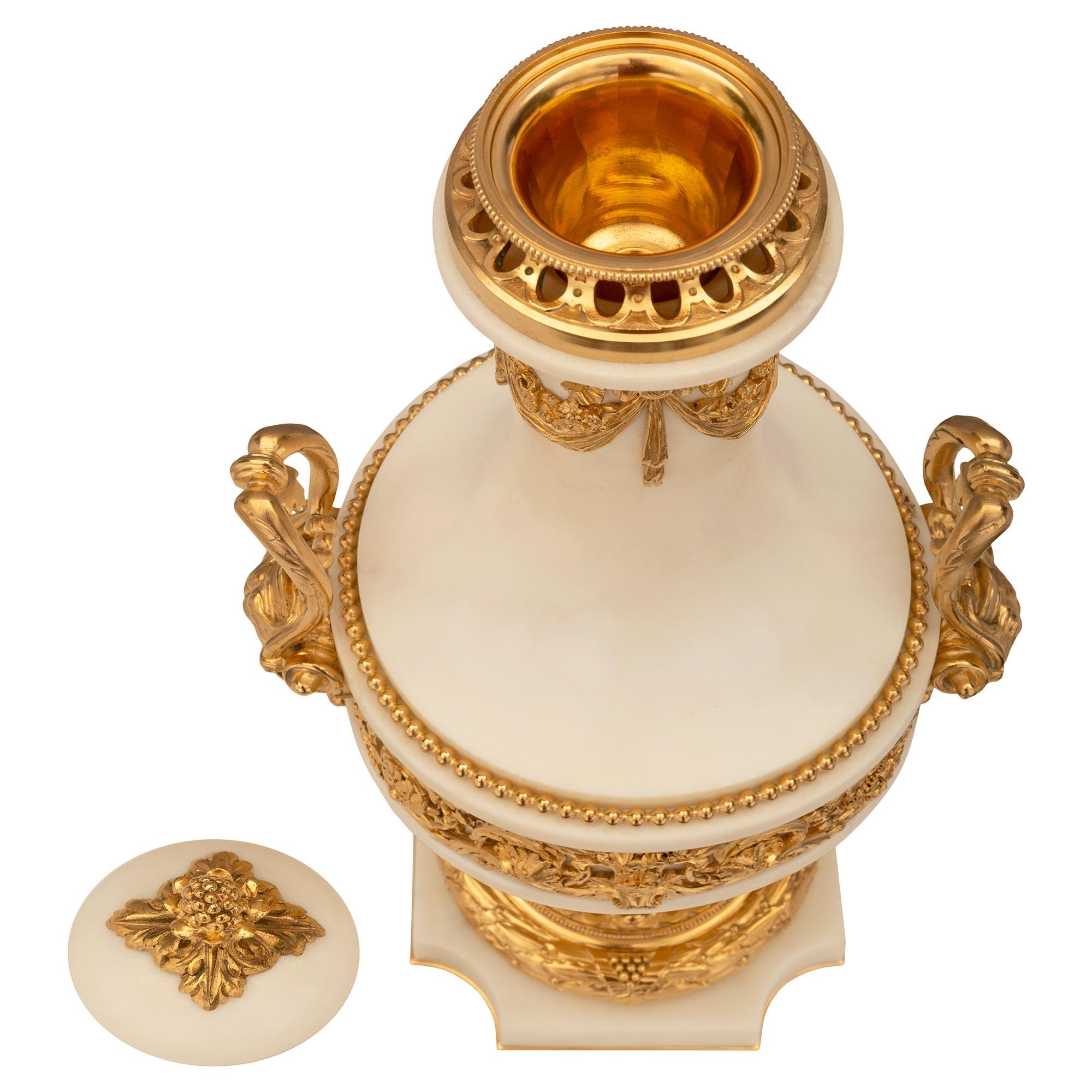 An exceptional and very high quality pair of French 19th century Louis XVI st. Belle Époque period white Carrara marble and ormolu lidded urns. Each urn is raised by a square base with concave corners and a fine bottom ormolu fillet. The socle