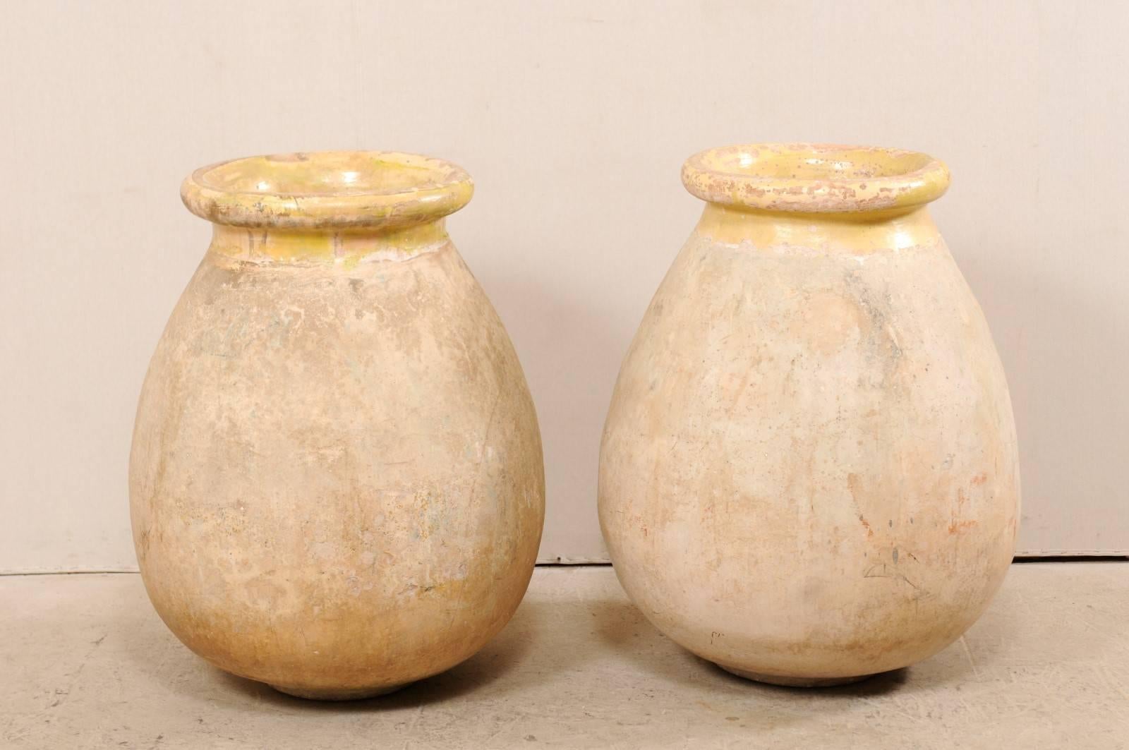 A pair of French 19th century Biot jars. This pair of antique French olive jars from Biot, France (a small potting village in the south of France) are made from terracotta with much of the original pale yellow glaze remaining about their neck and