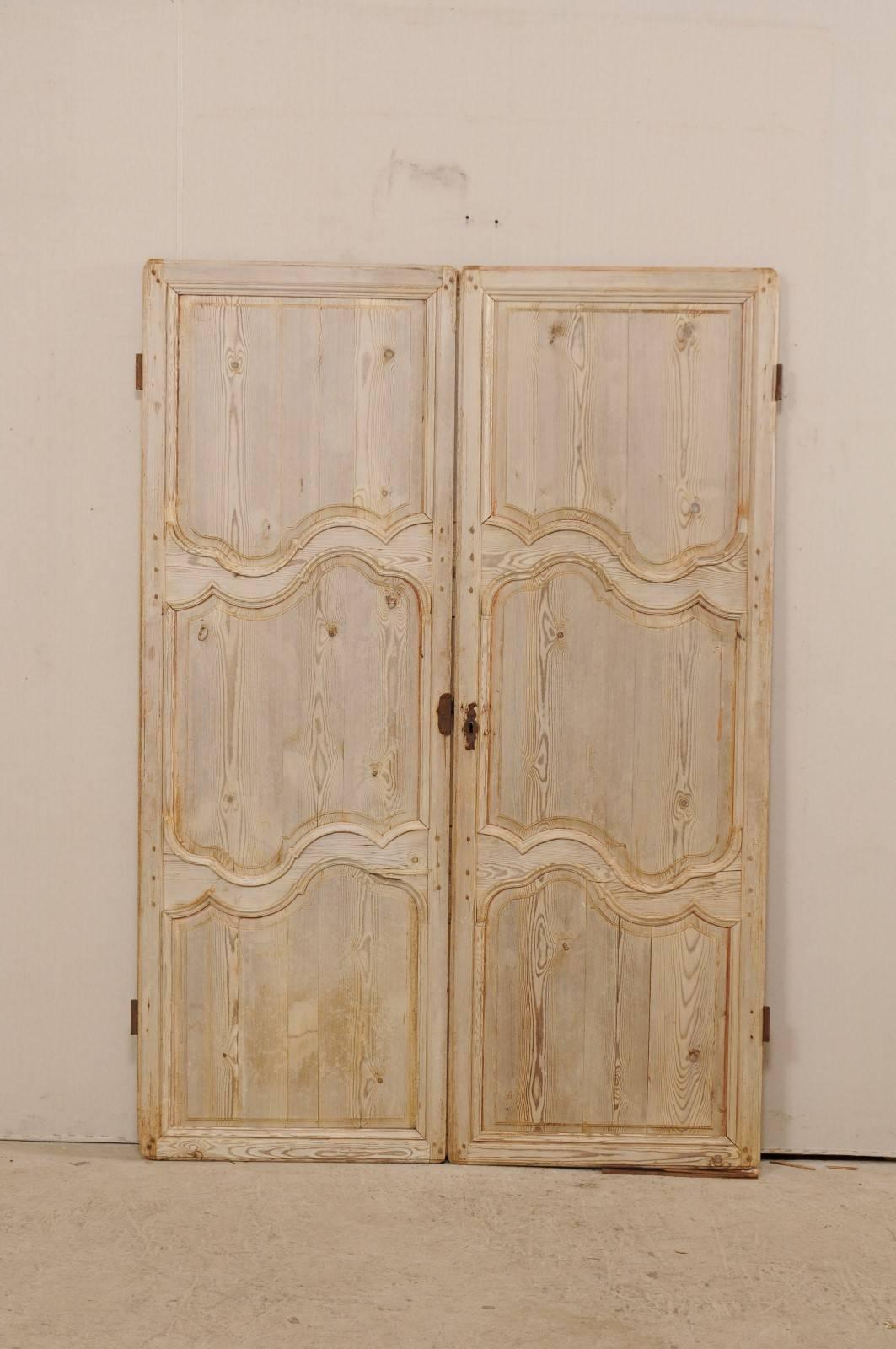 A pair of French bleached wood doors from the 19th century. This pair of French doors each feature three recessed panels, which have a sweetly carved curvy edging along the middle trim sections of the panel. The doors have a pale, bleached wood
