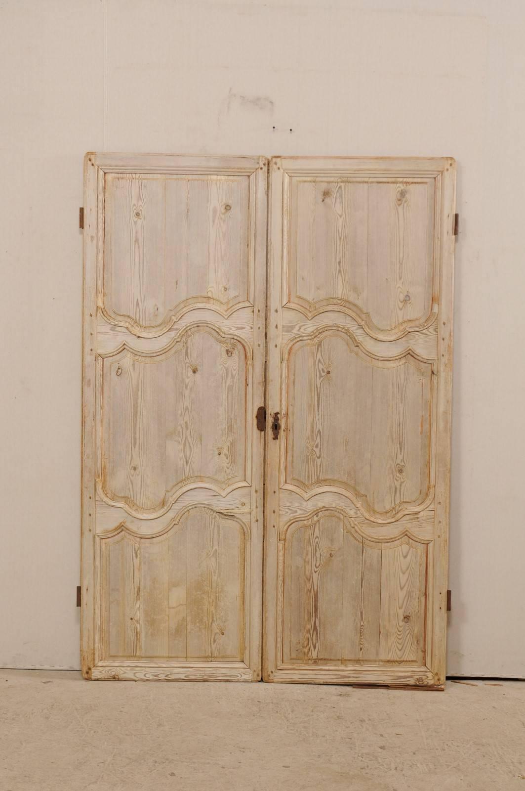 Une paire de portes françaises en bois blanchi du 19ème siècle. Cette paire de portes-fenêtres comporte trois panneaux en retrait:: dont la partie centrale est ornée d'une bordure curviligne joliment sculptée. Les portes ont une finition en bois