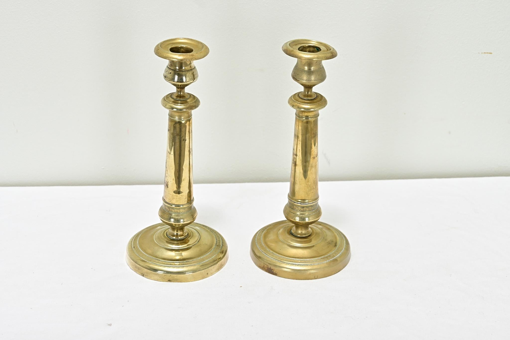 A pair of quality brass candlesticks from the 1800’s have a rich, smooth patina. You’ll find etched patterns and hatching at the top and base of each candlestick. View all the detailed images to see the current condition.