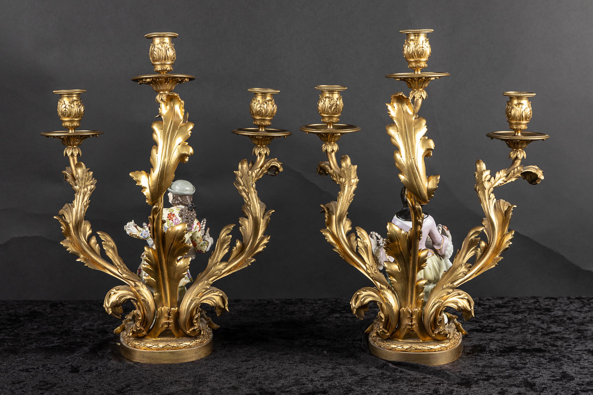 Gorgeous pair of French 19th century three-light bronze d’ore` candelabra with Meissen porcelain man on one, lady on the other: each modeled standing holding a handled basket. Each porcelain features features floriate details and rests on a bronze
