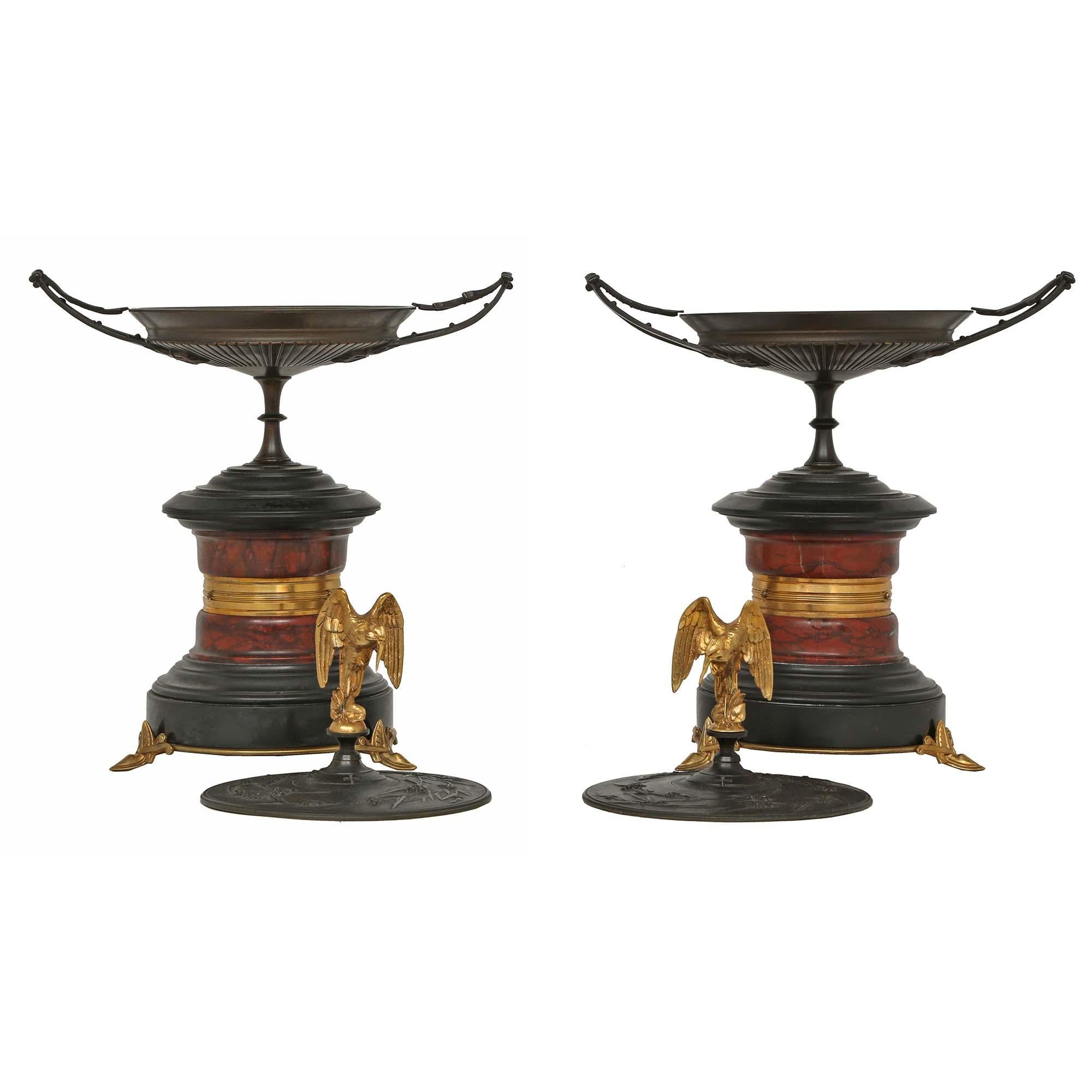 A Fine pair of French 19th century, bronze, marble and ormolu tazzas, with lids. The pair are raised by Egyptian designed ormolu supports below a black Belgian, red and black veined marble column, with an ormolu band. The urns, with laurel curved