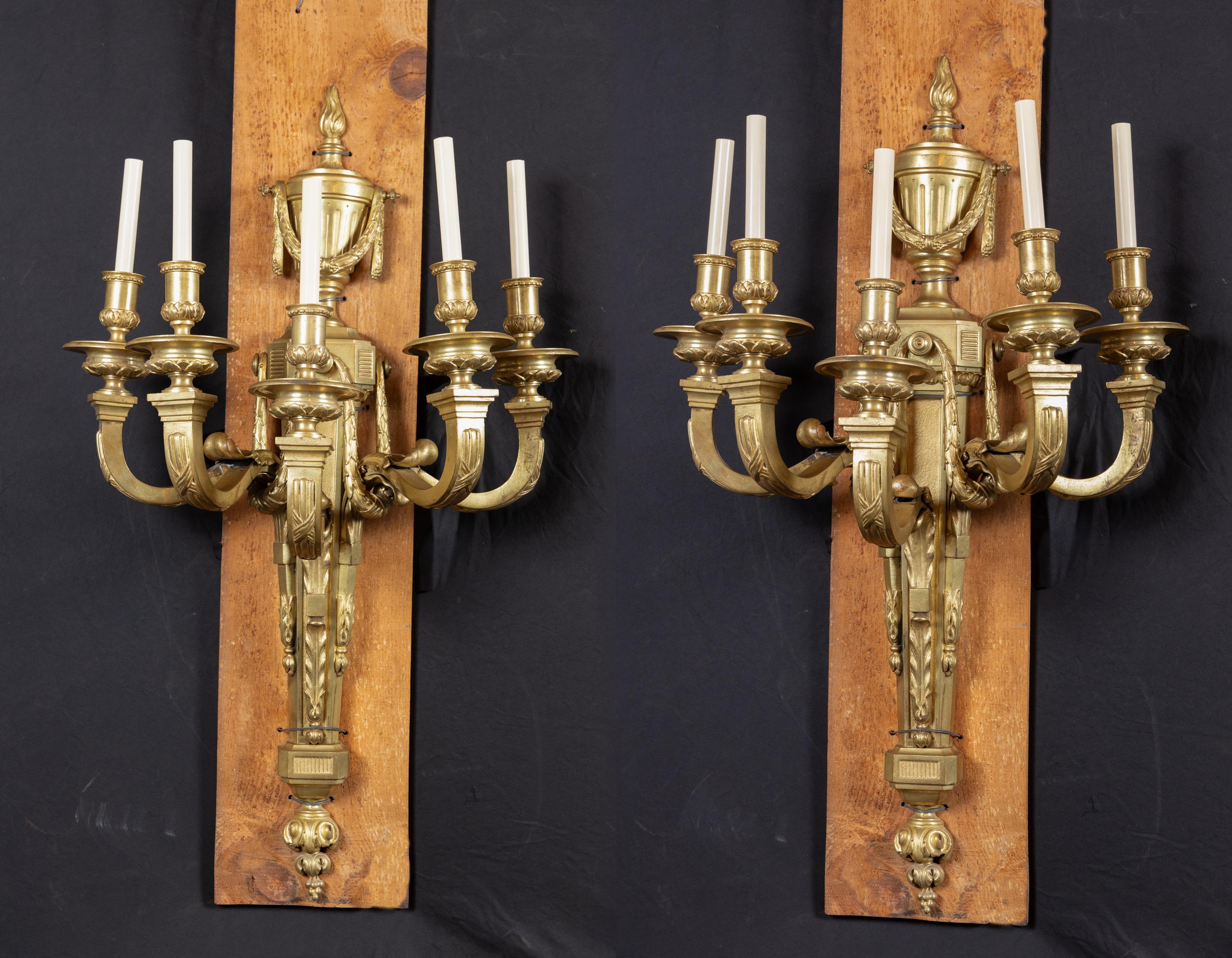 Grande paire d'appliques en bronze Louis XVI du 19ème siècle avec urne drapée de guirlandes. Chaque pièce est surmontée d'une flamme et accueille cinq bras. Remarquez les détails de la barbichette ainsi que le motif en tissu sur chaque bras. D'une