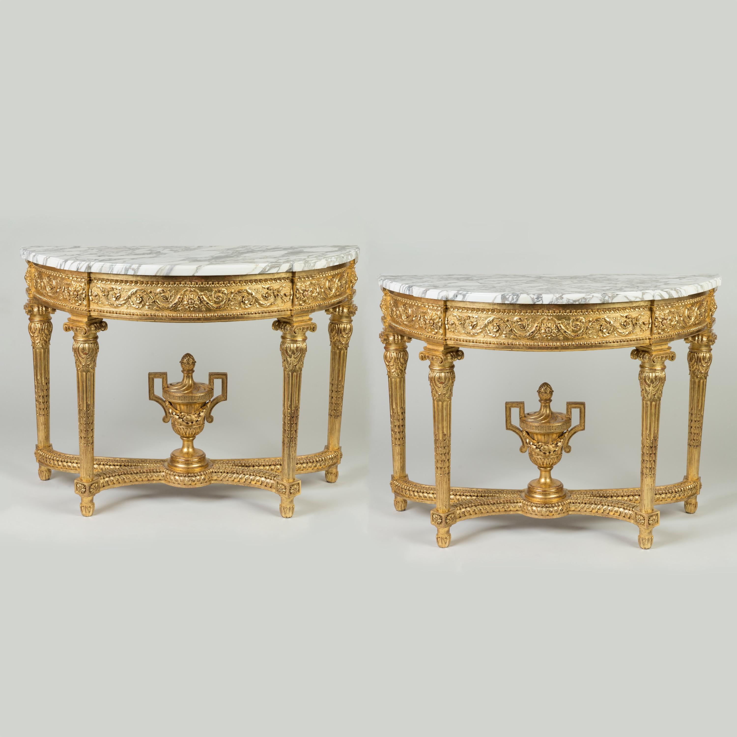 An Important Pair of Stately Console Tables
In the Louis XVI Manner

Constructed in carved and gilded wood; rising from four stop-fluted legs adorned with lotus bud forms and terminating in ionic capitals; having conjoining stylised 'X' form
