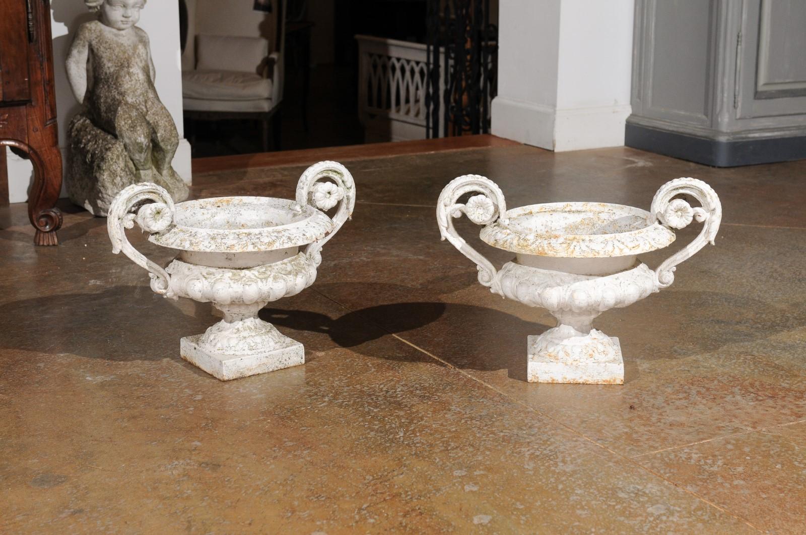 A pair of French cast iron vases from the 19th century, with white painted finish and large voluted handles. Created in France during the 19th century, each of this pair of vases draws our attention with its nicely weathered appearance and delicate