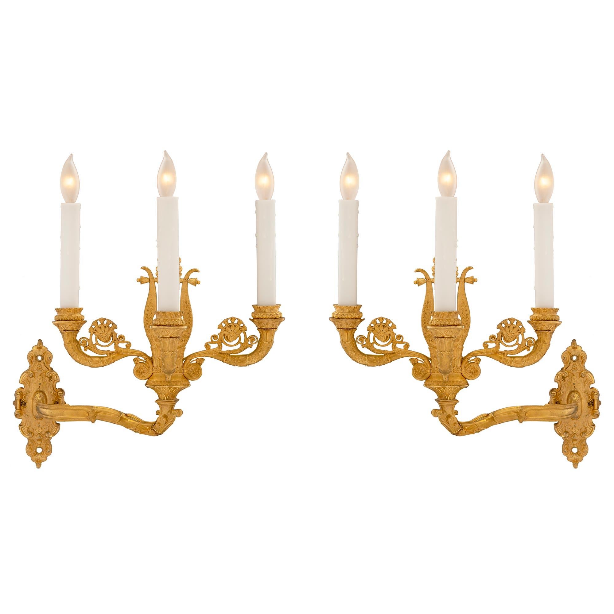 A stunning true pair of French early 19th century Charles X Period ormolu three arm Bras de Lumière sconces. Each high quality sconce displays a beautiful scrolled foliate back plate with an intricately hammered design all in a striking satin and