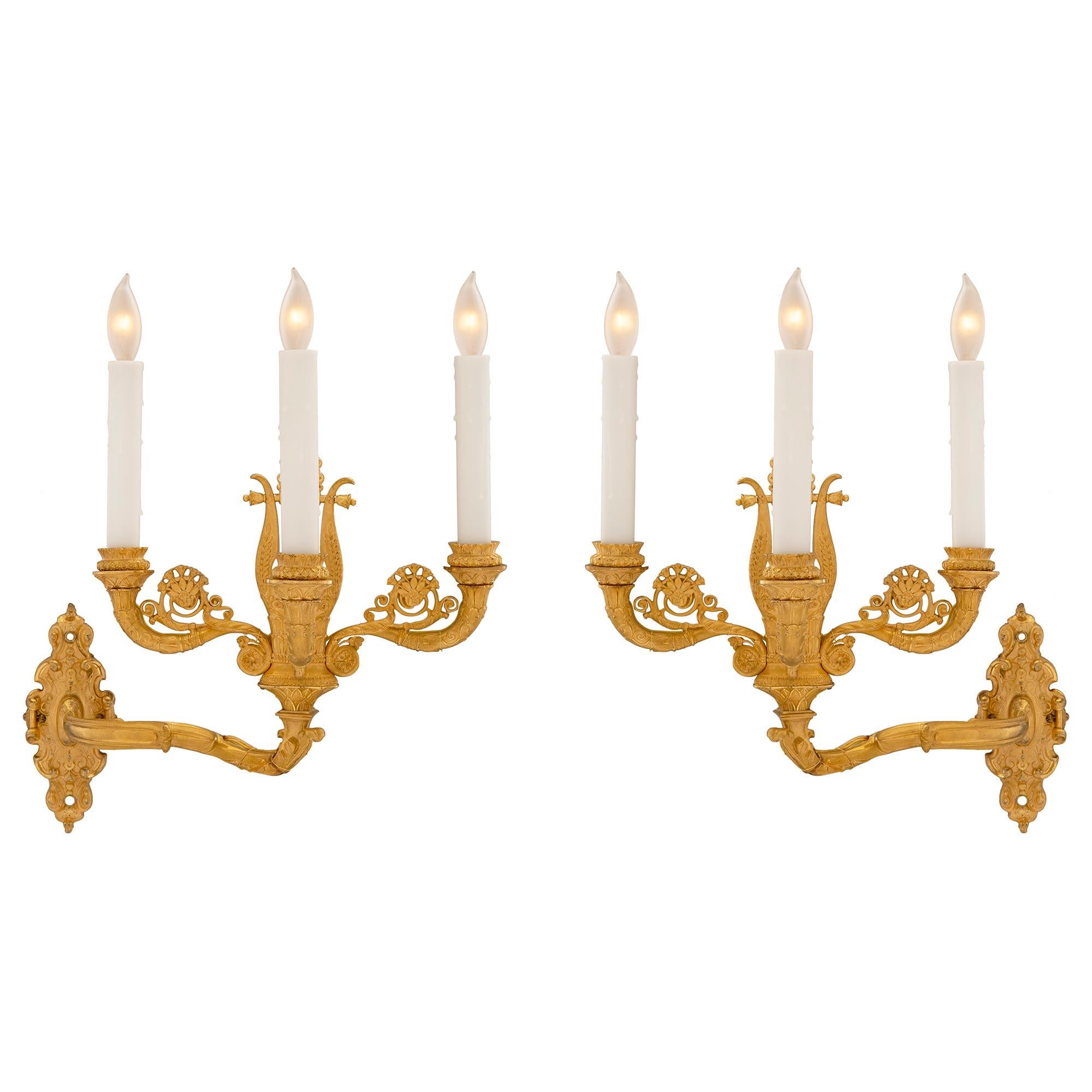 Impresionante pareja de apliques franceses de tres brazos Bras de Lumière ormolu de principios del siglo XIX. Cada candelabro de alta calidad presenta una hermosa placa posterior foliada con un intrincado diseño martillado, todo ello en un llamativo