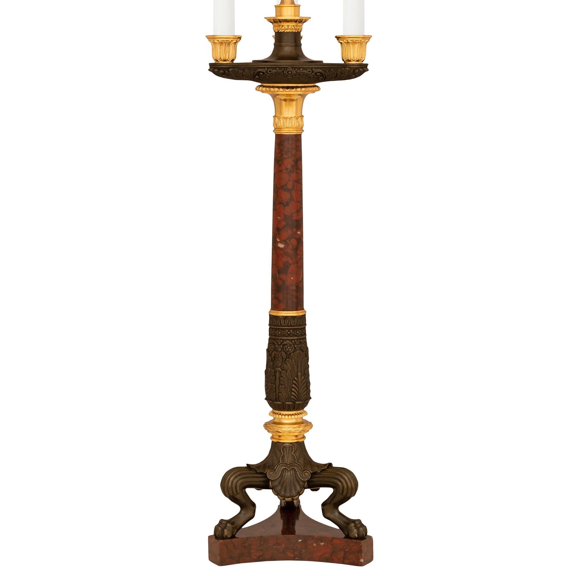 A stunning pair of French 19th century Charles X st. Rouge Griotte marble, Ormolu, and patinated Bronze candelabra lamps. Each wonderful three arm lamp with two central electrified lights is raised by a triangular Rouge Griotte marble base with