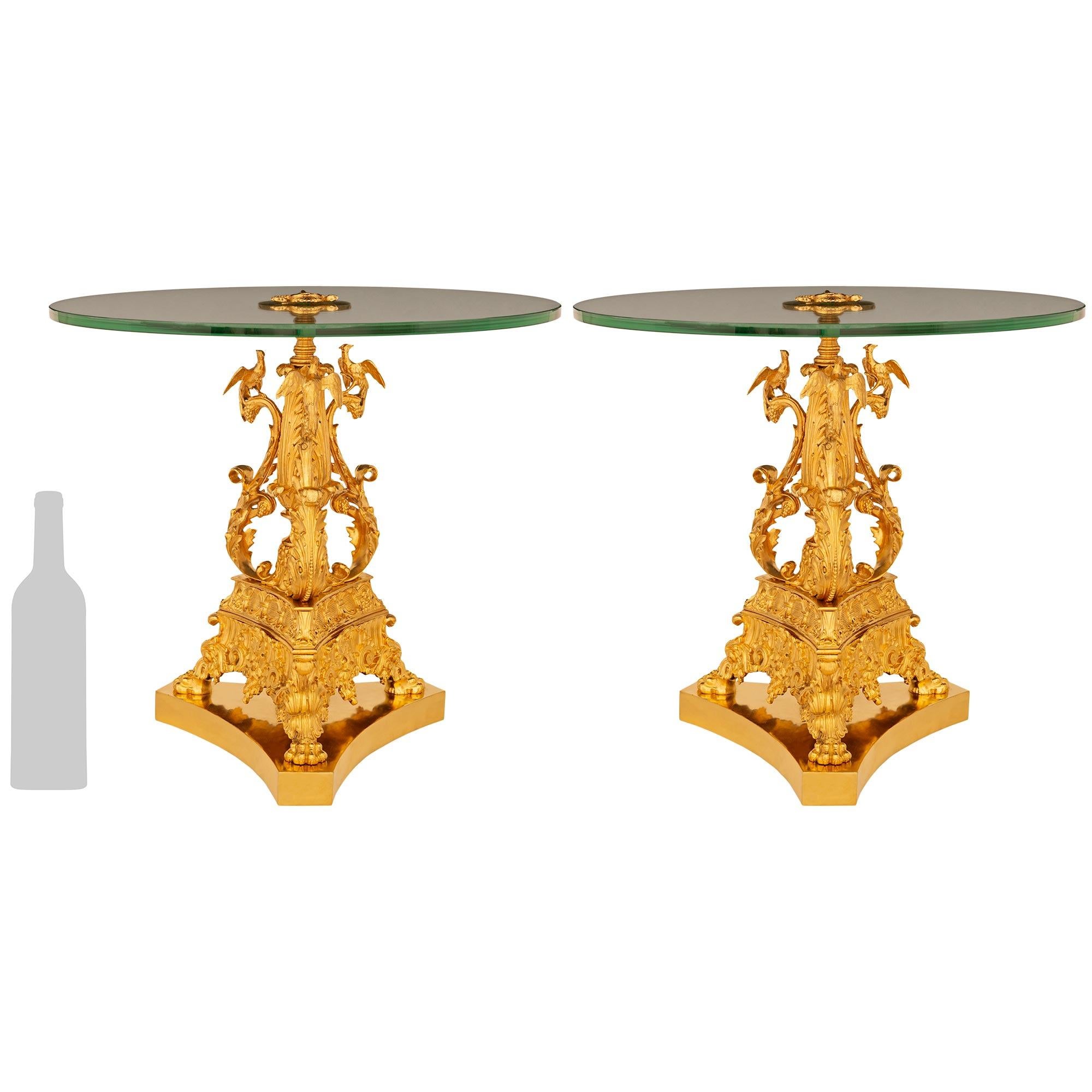 Une étonnante et très impressionnante paire de tables basses/de chevet en bronze doré et verre du XIXème siècle. Chaque table, élaborée et de grande qualité, repose sur trois pieds décorés de rinceaux et de feuillages, avec des pieds en forme de