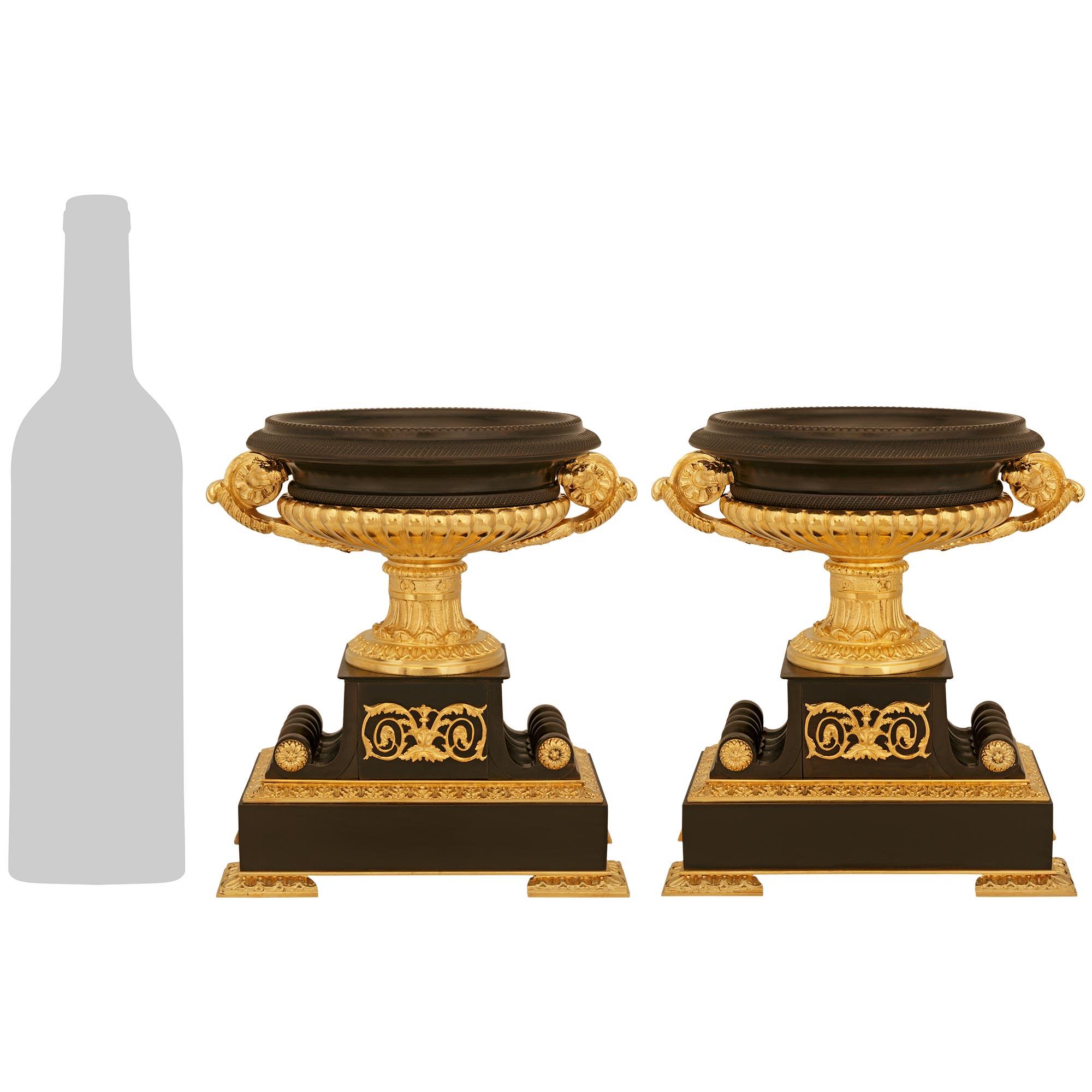 A handsome and high quality pair of French 19th century Charles X st. Ormolu and patinated Bronze urns. Each exceptional urn is raised on a rectangular patinated Bronze plinth supported on four Rais de Coeur decorated feet. A Rais de Coeur band