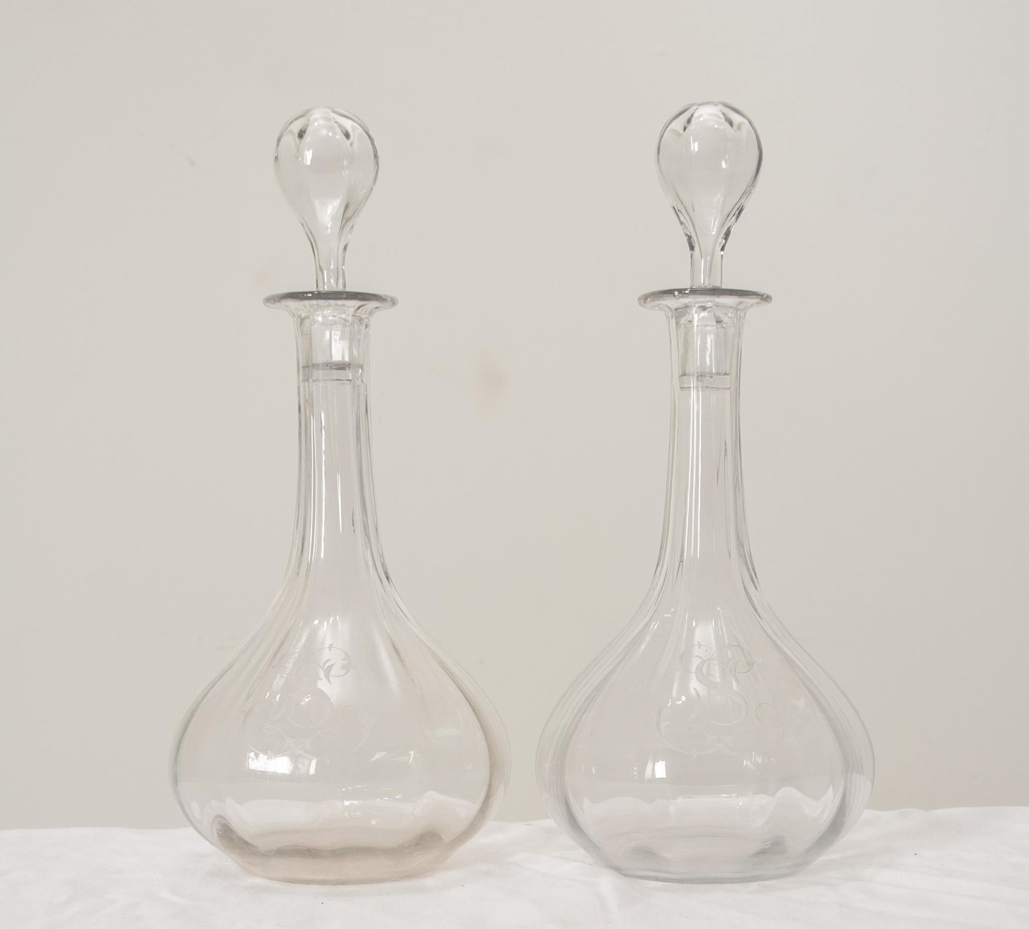 A charming set of 19th century hand blown glass decanters from France featuring clear rippled crystal glass in  fluted designs with rounded bases and elegant matching stoppers. The letter “S” is finely etched on each decanter in the center with a