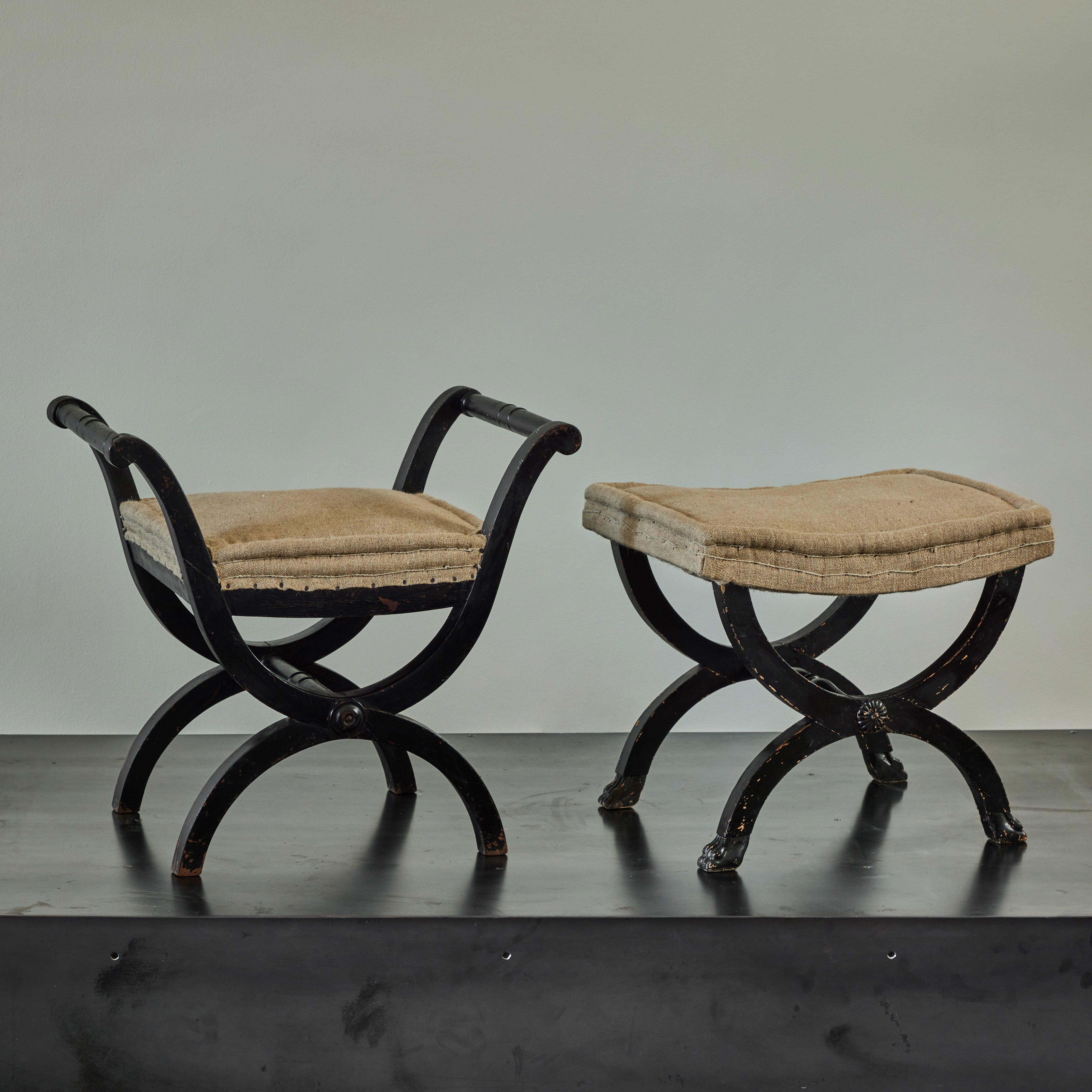 Pair of French 19th century harlequin-style curule stools or benches with ebonized wood framework and raw flax-toned linen upholstery. With elegant sloping lines and comfortable cushioning, the set brings a quality of relaxed glamour to any space.