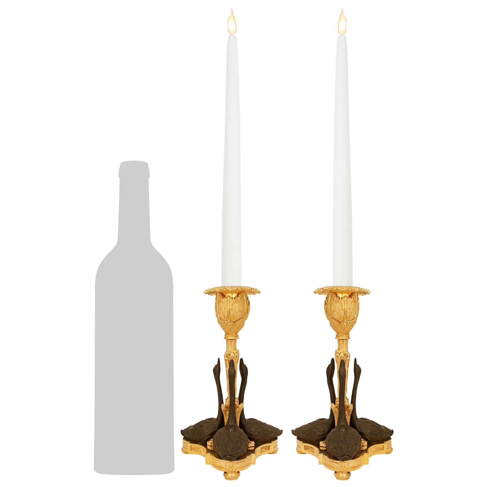 Una coppia elegante e finemente dettagliata di candelieri francesi del XIX secolo in bronzo patinato e Ormolu. Ogni candeliere è sollevato da una base triangolare con lati concavi e pannelli incassati, mentre è sostenuto da tre piedi a sfera