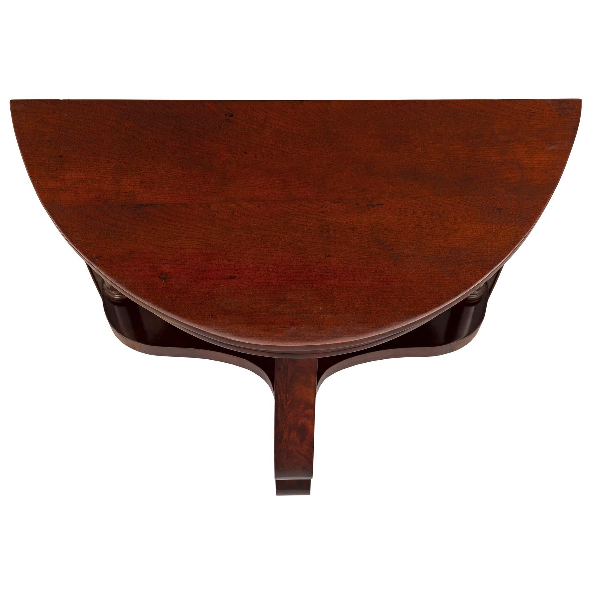 Un'elegante coppia di consolle in mogano specchiato in stile Impero del XIX secolo. Ogni console a forma di demi-lune è sollevata da due piedini a forma di topie screziati su ciascun lato e da un bellissimo supporto centrale a volute che conduce al