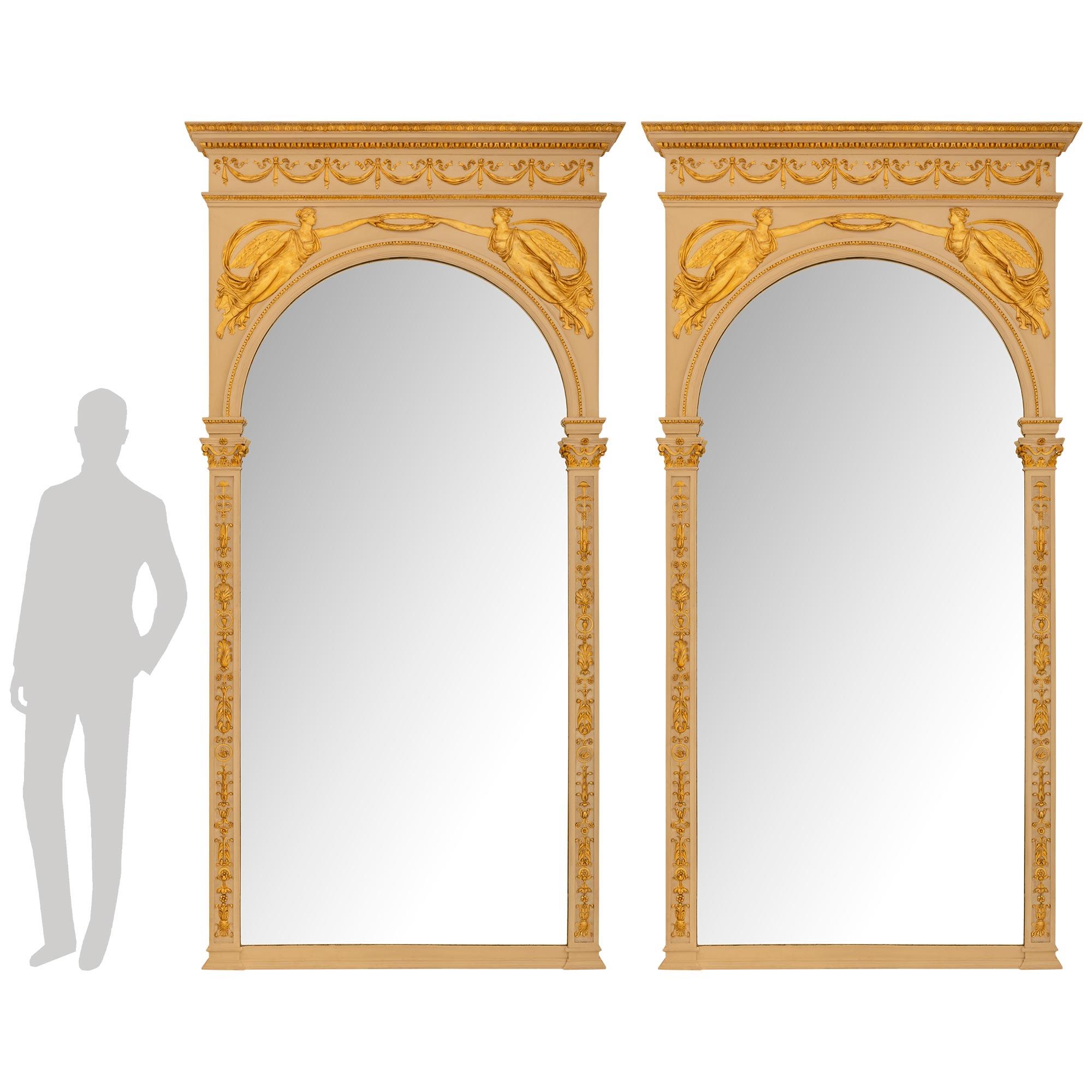 Une paire impressionnante et architecturale de miroirs en bois patiné et doré de style Empire du 19ème siècle. Chaque miroir aux dimensions généreuses, avec ses plaques d'origine, repose sur une base droite tachetée, flanquée de chaque côté de pieds