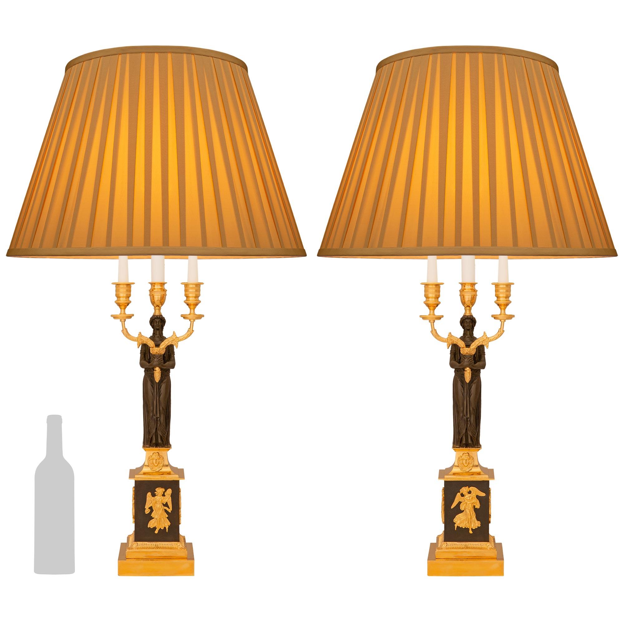 Une élégante paire de lampes candélabres en bronze patiné et bronze doré de style Empire du 19e siècle. Chaque candélabre à trois bras monté dans une lampe est monté sur un socle carré en bronze doré avec un bandeau supérieur cannelé. Le support